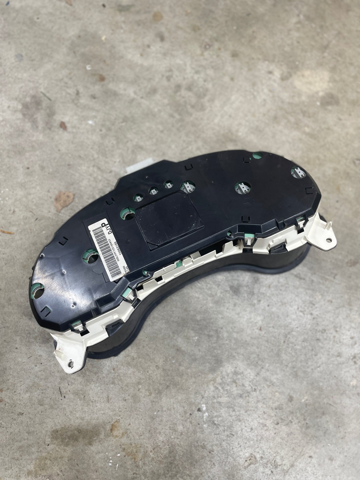 A General Motors OEM Tested Instrument Cluster with Tachometer for 2001-2005 Chevy S10 or Blazer with Console Shifter lies face down on a gray concrete floor, showing screws and a barcode label.