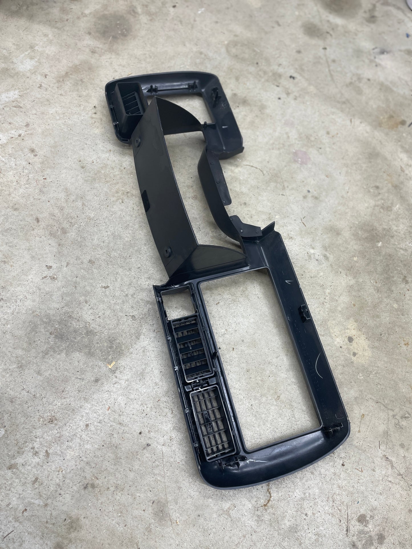 A General Motors OEM Instrument Cluster Dash Bezel in dark gray for 1995-1997 Chevy S-10 and Blazer, with vent openings and mounting slots, is pictured cleanly on a concrete floor, photographed from above.