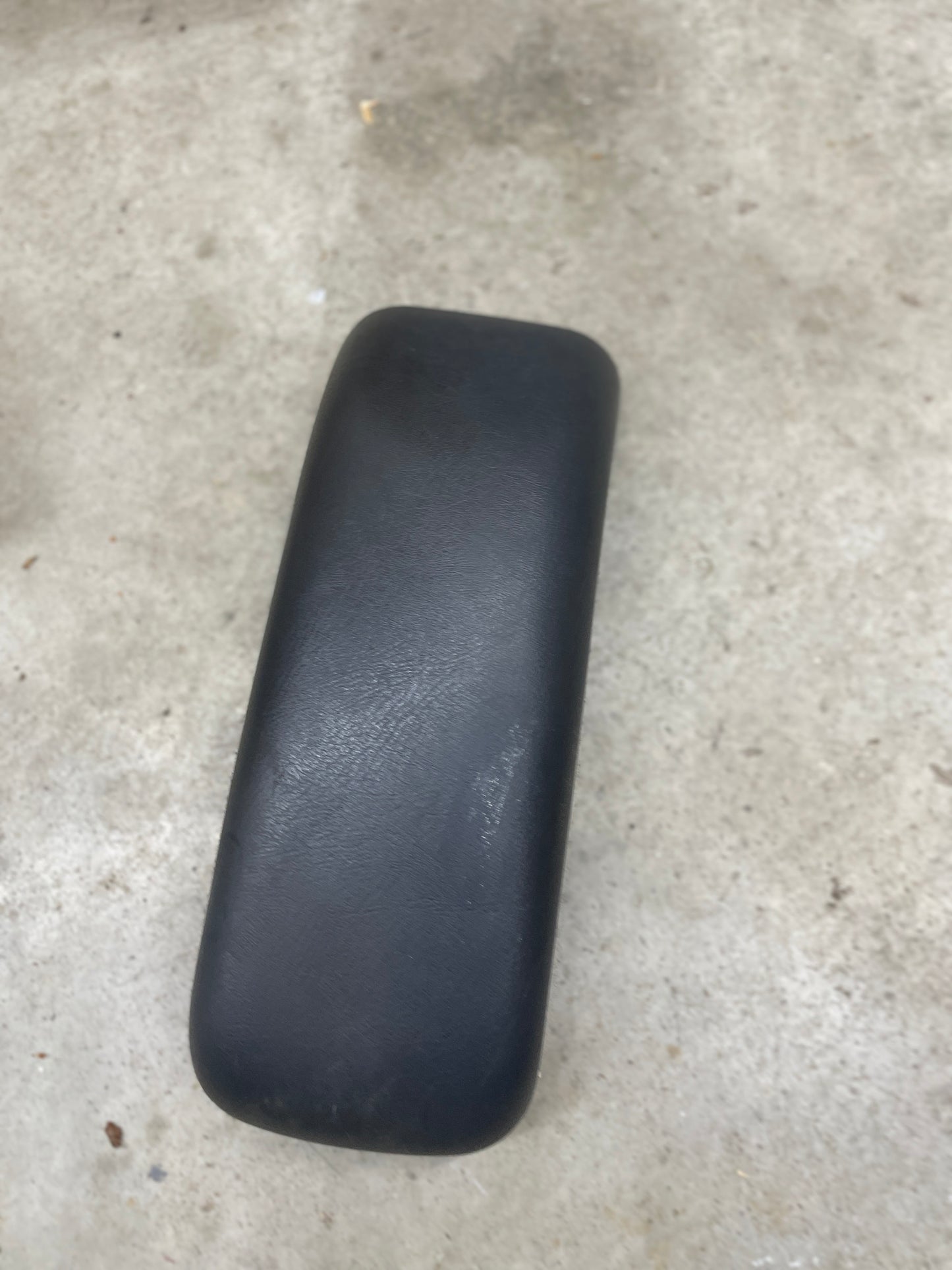 A General Motors OEM Center Lid Armrest in dark gray for 1996-2005 Chevy S10 and Blazer auto trans shifter consoles is lying on a textured light gray concrete surface.