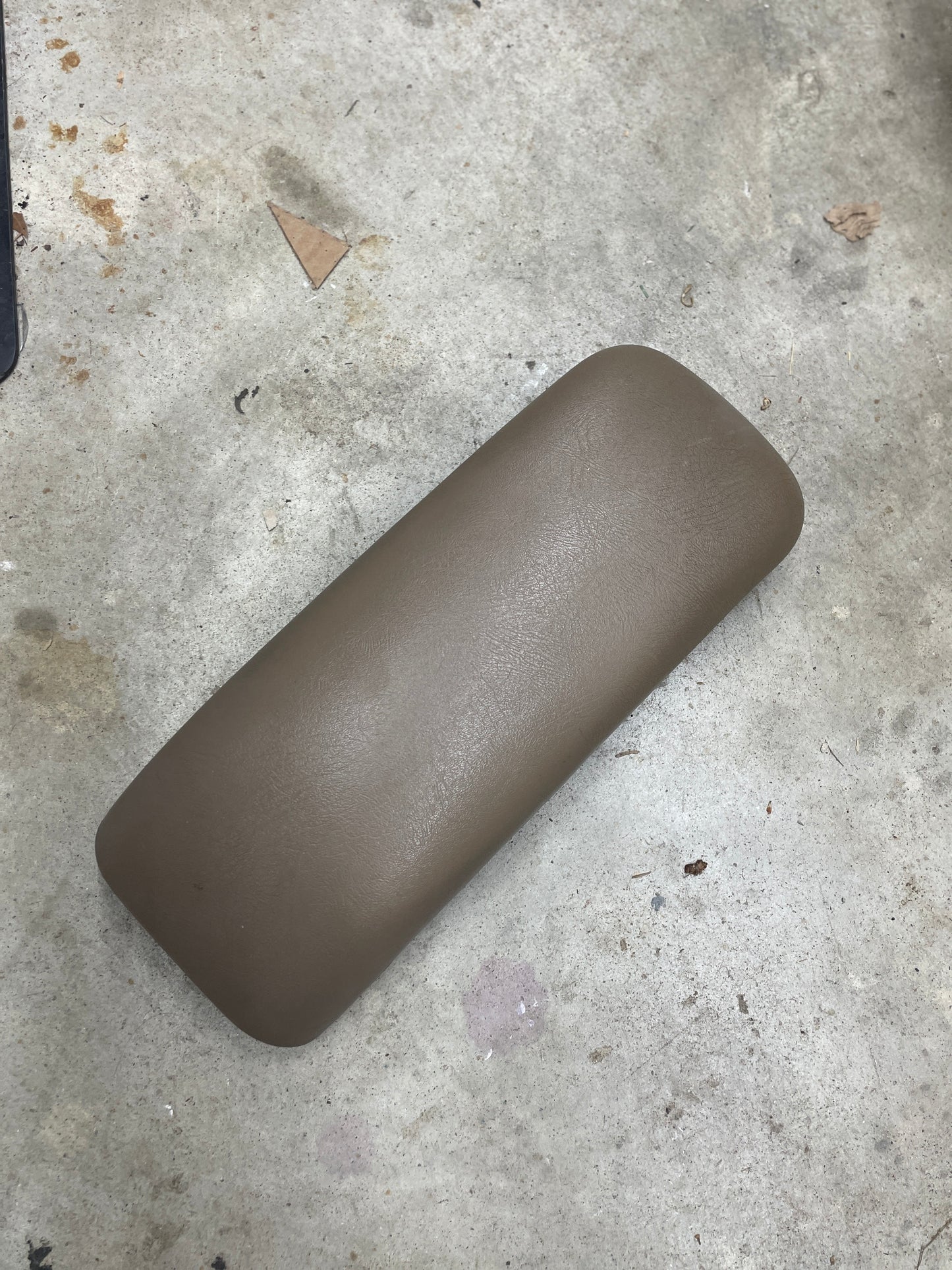 A tan OEM Center Lid Armrest by General Motors, designed for auto trans shifter consoles in 1996-2005 Chevy S10, Blazer, and more, rests on a rough concrete floor—ideal as a replacement for your vehicle’s original armrest.