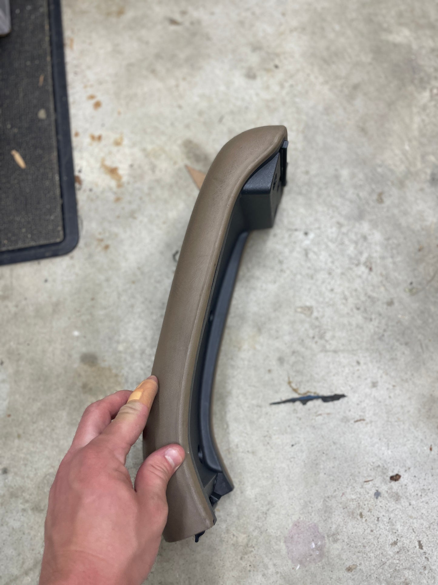 A hand displays the General Motors OEM Center Lid Armrest in Tan for the Auto Trans Shifter Console (1996-2005 Chevy S10, Blazer, and more) against a concrete floor background.