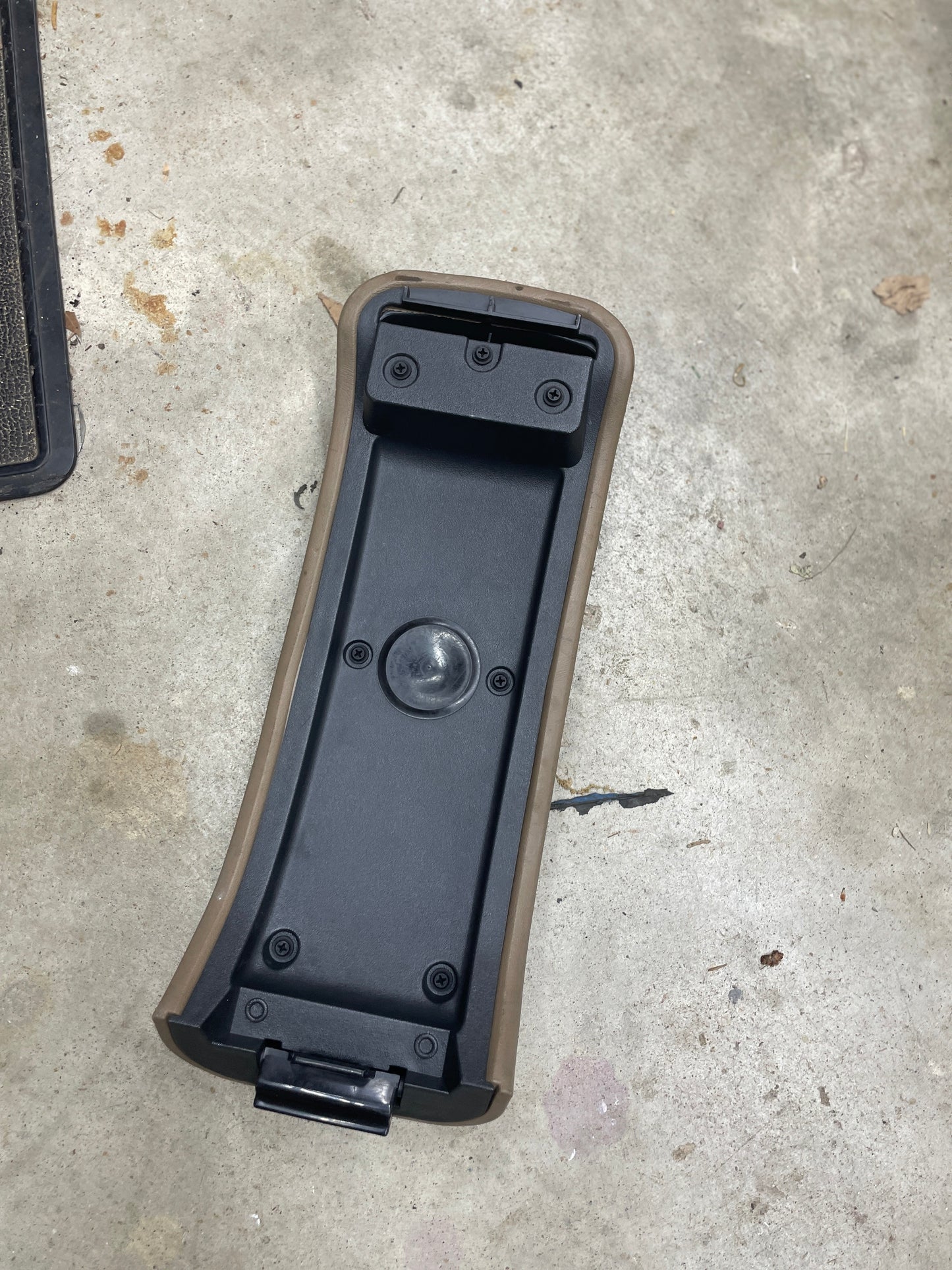 A tan OEM Center Lid Armrest for auto trans shifter console (1996-2005 Chevy S10, Blazer, and more) by General Motors lies on a concrete floor with debris—ideal as a replacement part.