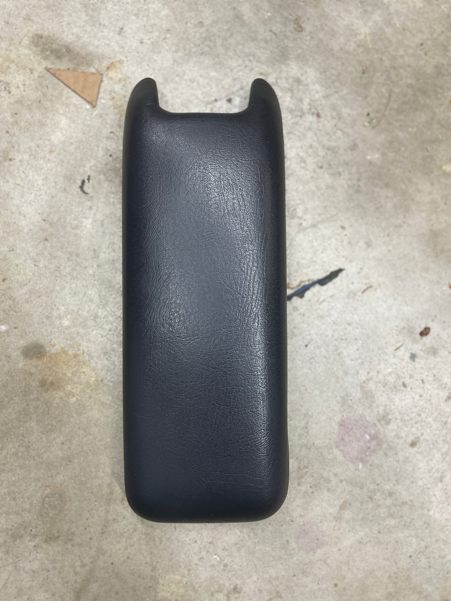 A General Motors OEM Center Console Lid Armrest in dark gray for 1994-1997 Chevy S10, Blazer, and more rests on a speckled concrete surface.