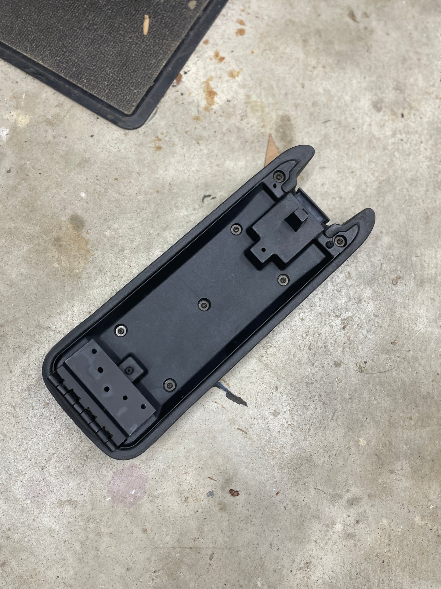 A General Motors OEM Center Console Lid Armrest in dark gray for 1994-1997 Chevy S10, Blazer, and more sits on a concrete floor near the edge of a black mat.