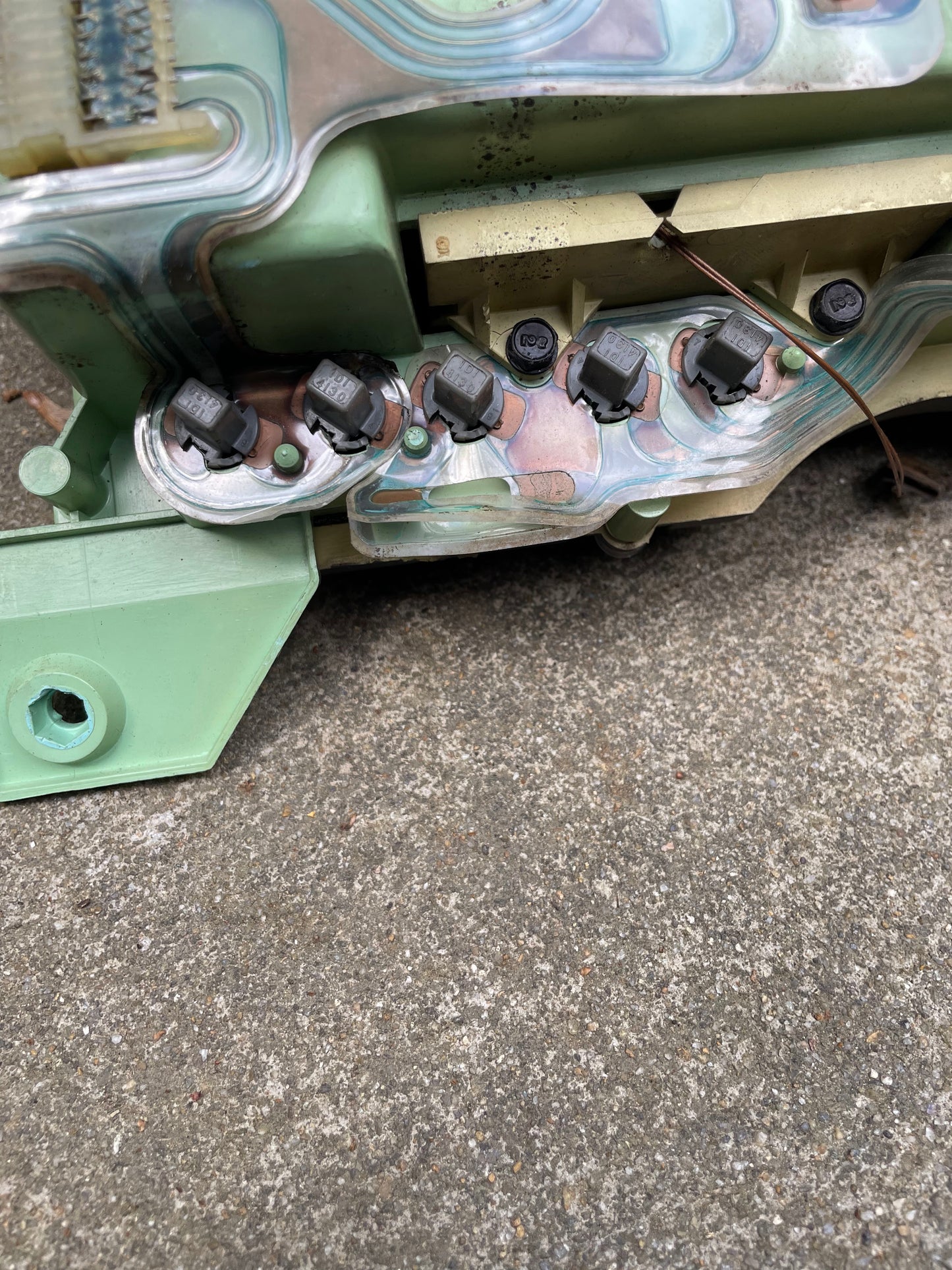 Close-up of a green circuit board with five black components from a General Motors OEM Instrument Cluster with Mechanical Speedo & PRNDL for 1986-1989 Chevy S10 Blazer, on concrete. A brown wire hints at its mechanical speedometer function.