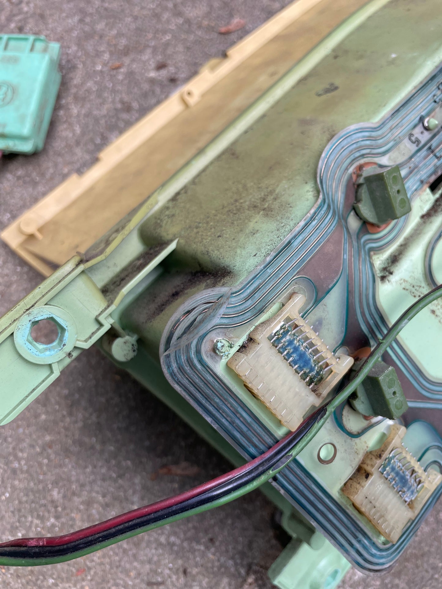Close-up of a weathered General Motors OEM Instrument Cluster with Mechanical Speedo & PRNDL for 1986-1989 Chevy S10 Blazer, showing discolored connectors and exposed wiring on a concrete surface. Some plastic parts appear worn.