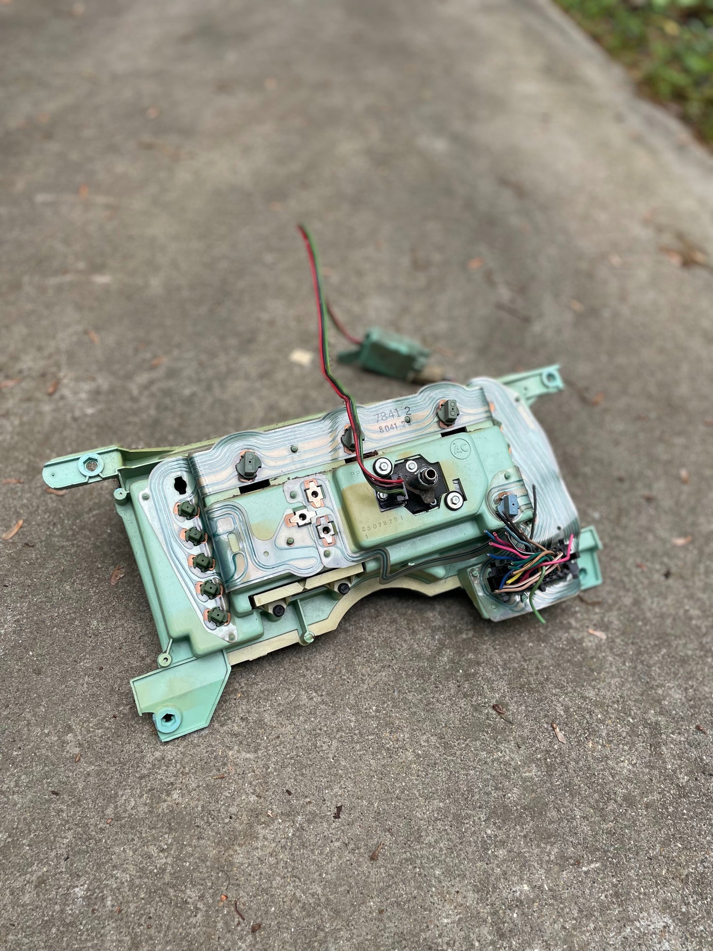 A General Motors OEM Instrument Cluster with Mechanical Speedo for 1986-1990 Chevy S10 Blazer and manual transmission is shown outdoors on concrete, green/silver circuit board and wires attached, with grass visible nearby.