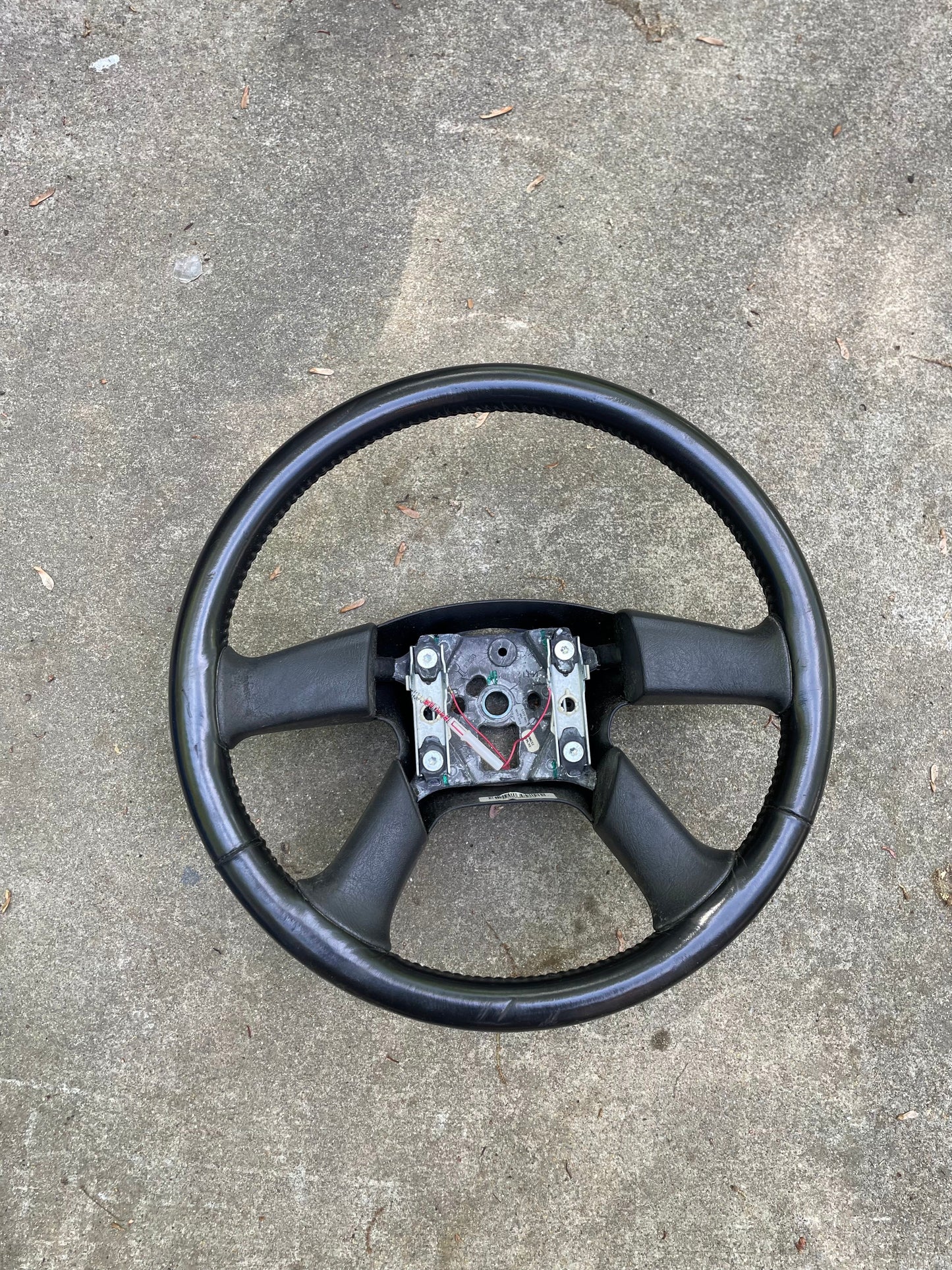 An OEM Leather Steering Wheel by General Motors for 2002-2009 Chevy Silverado, Trailblazer, and more lies on rough gray concrete with exposed metal components.