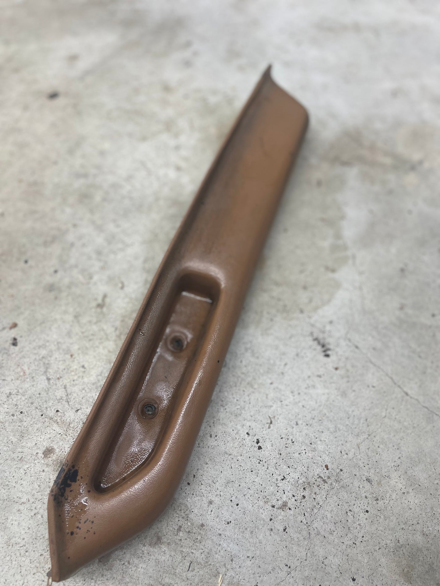 A beige OEM passenger door panel armrest handle by General Motors for 1986-1993 Chevy S10, Blazer, and more lies on a stained concrete surface.