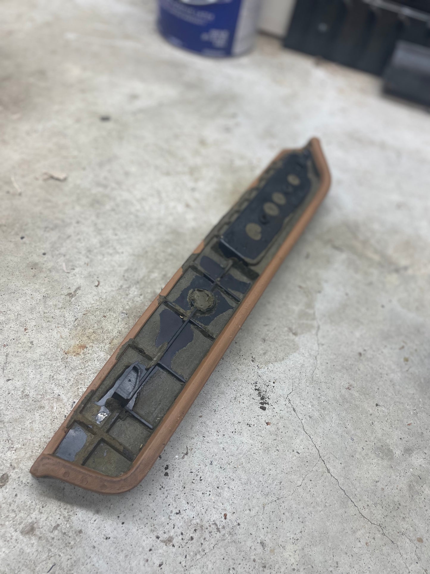 An OEM Passenger Door Panel Armrest Handle in beige by General Motors for 1986–1993 Chevy S10, Blazer, and more rests on a dirty concrete floor, showing signs of wear and partial damage.