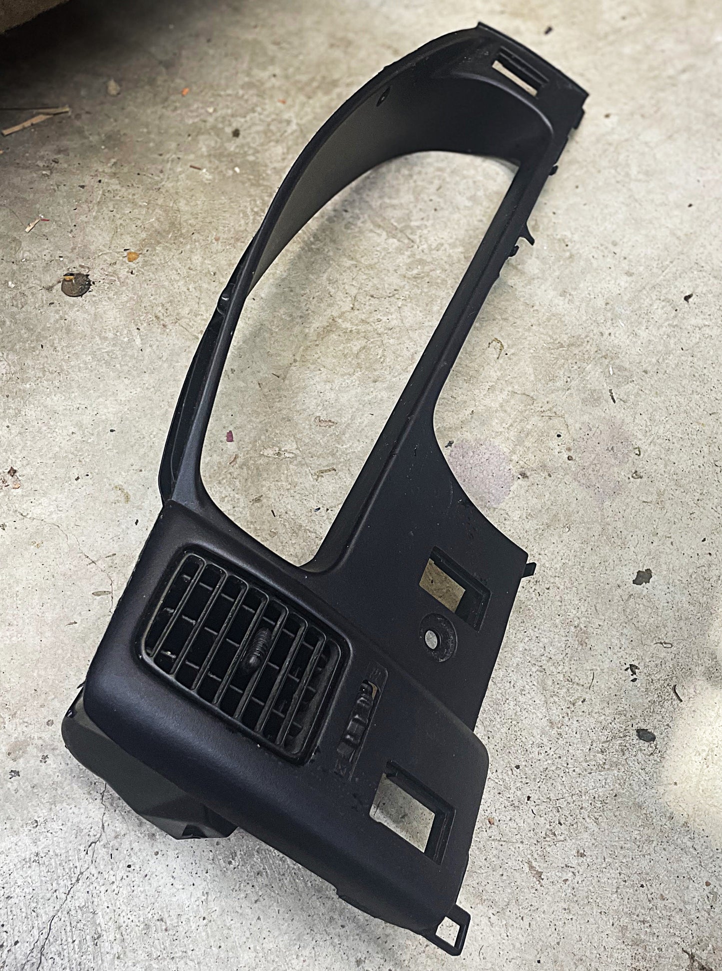 A General Motors OEM Instrument Gauge Cluster Dash Bezel for 1995-2004 Toyota Tacoma, featuring air vent and cutouts, is shown on a concrete floor.