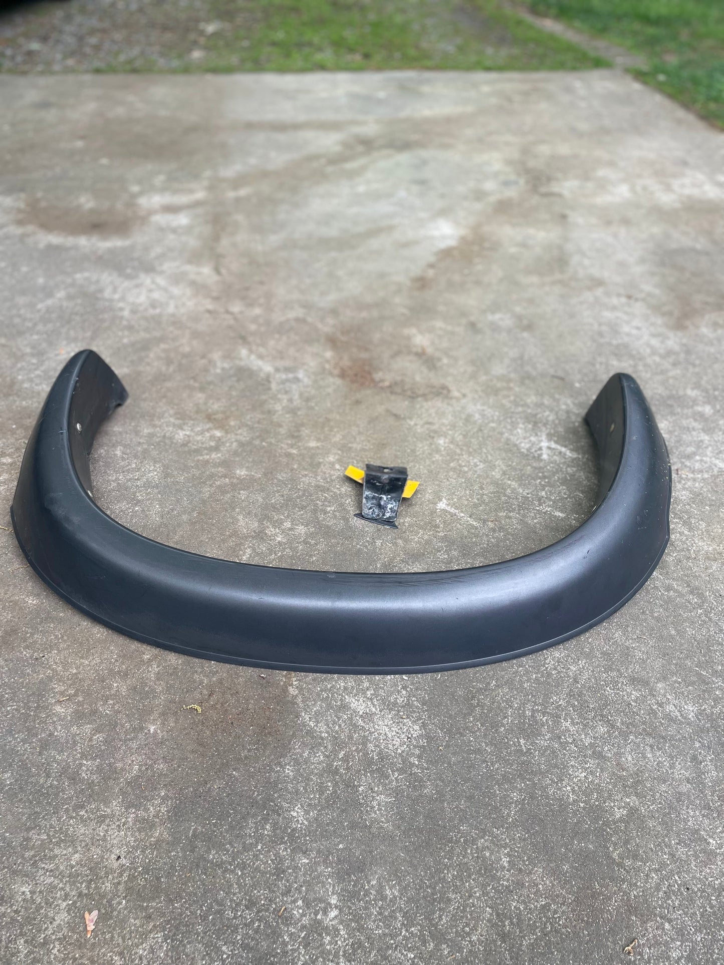 An OEM Rear Left Driver ZR2 Fender Flare Body Side Extension for 1995-2005 Chevy Blazer/GMC Jimmy by General Motors and a small yellow and black tool are on an outdoor concrete surface with grass in the background.
