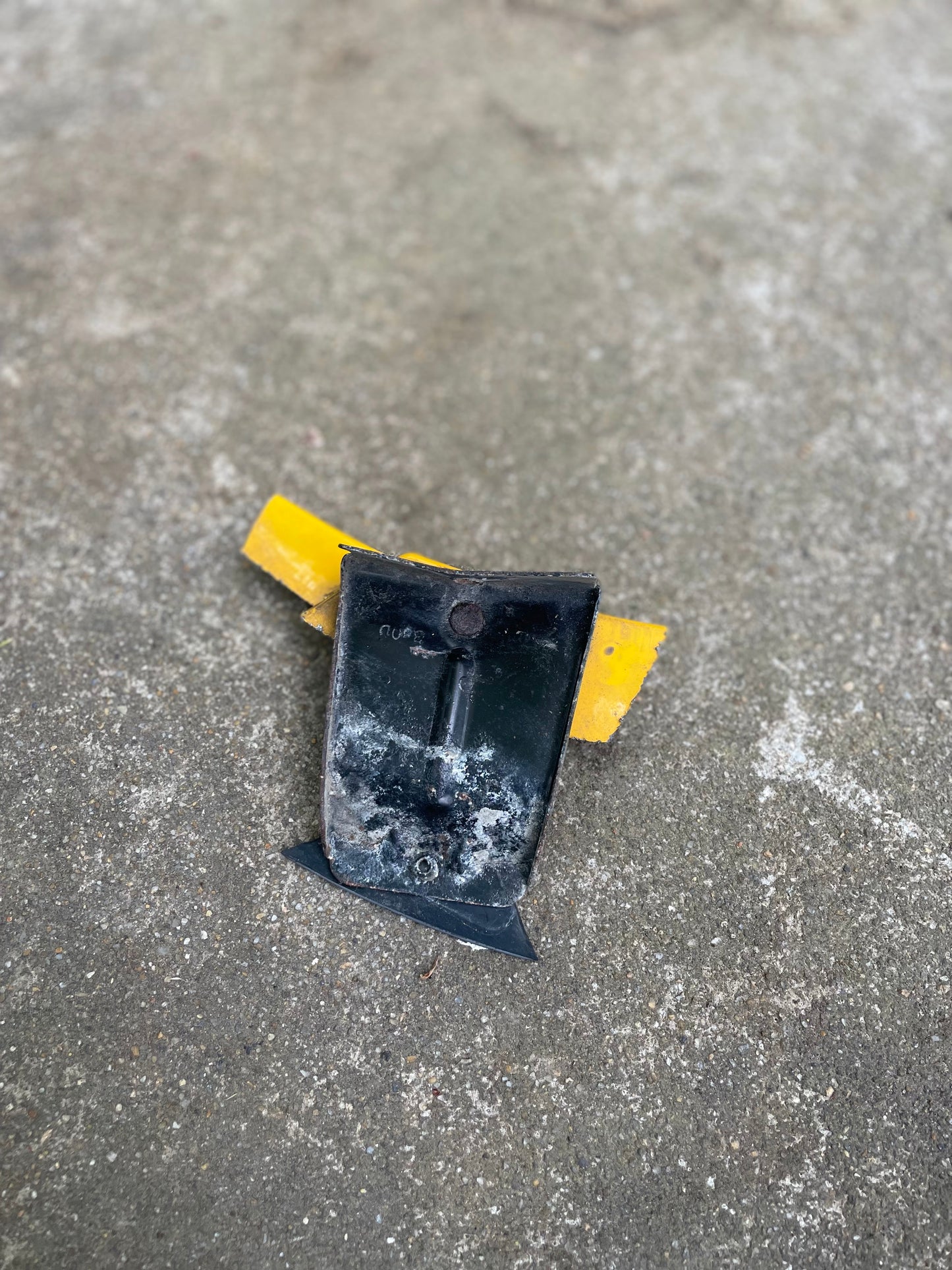 A damaged yellow and black road reflector rests on rough, gray concrete near an OEM Rear Left Driver ZR2 Fender Flare Body Side Extension for 1995-2005 Chevy Blazer or GMC Jimmy by General Motors. The reflector is weathered, dirty, and scratched.