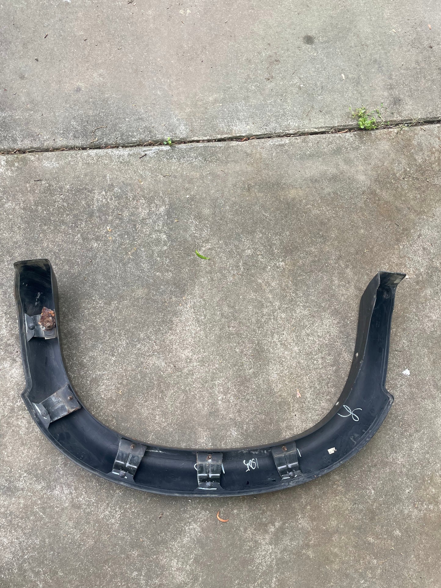 A General Motors OEM Rear Left Driver ZR2 Fender Flare Body Side Extension for 1995-2005 Chevy Blazer/GMC Jimmy rests on concrete, showing some rust and wear, with several mounting clips and markings visible.