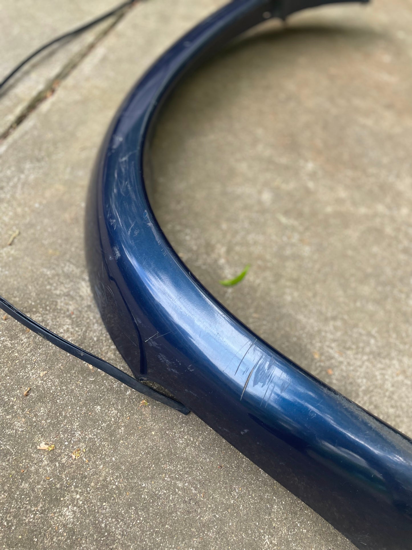 A General Motors OEM Front Right Passenger ZR2 Blue Fender Flare Extension for 1994-2005 Chevy S10/GMC Sonoma shows scratches and scuffs on a concrete surface, with a black cable partially visible beside it.