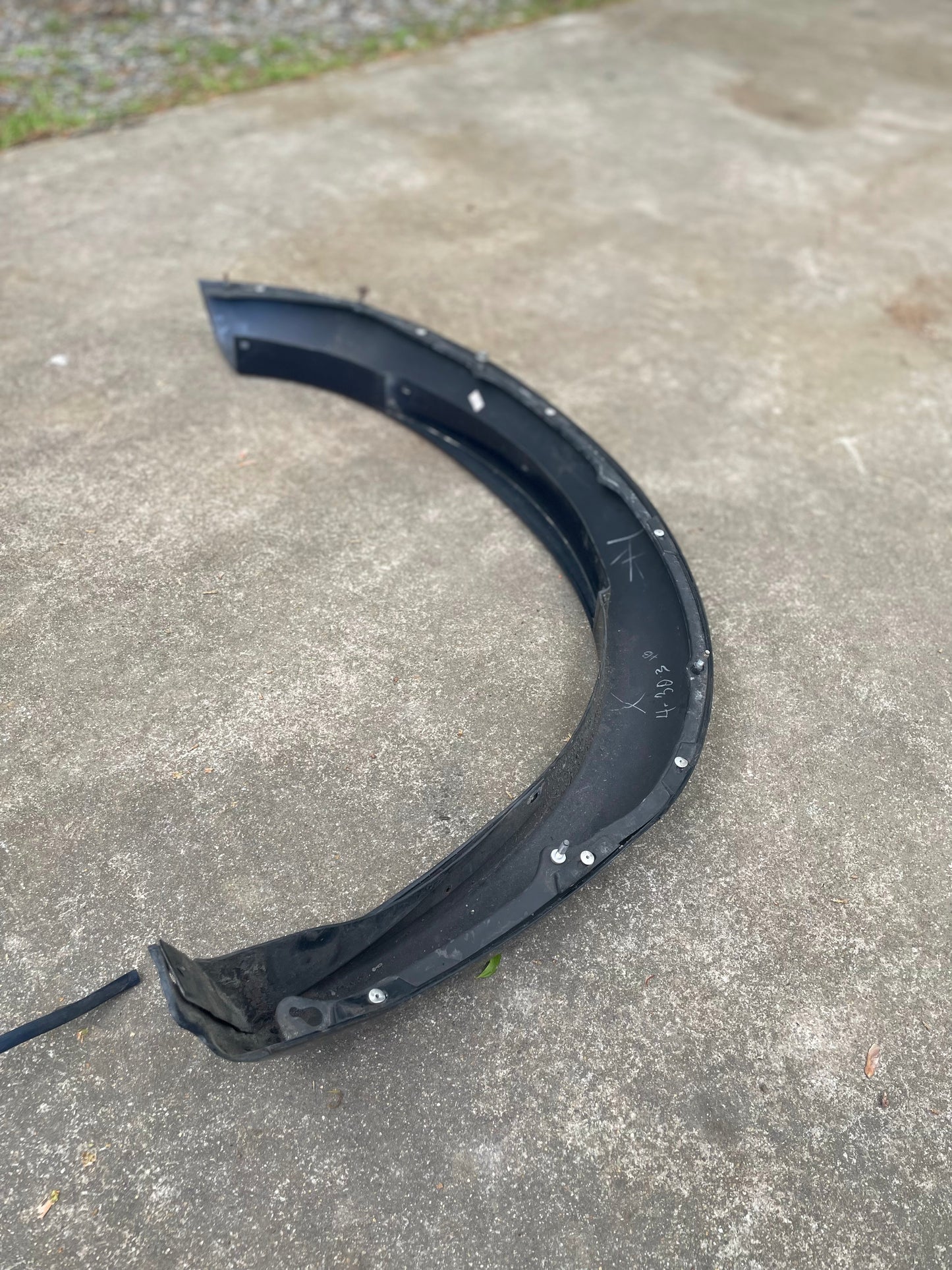 A blue OEM Front Right Passenger ZR2 Fender Flare Extension by General Motors for 1994-2005 Chevy S10 and GMC Sonoma lies detached on concrete outdoors, with grass in the background; it shows signs of wear.