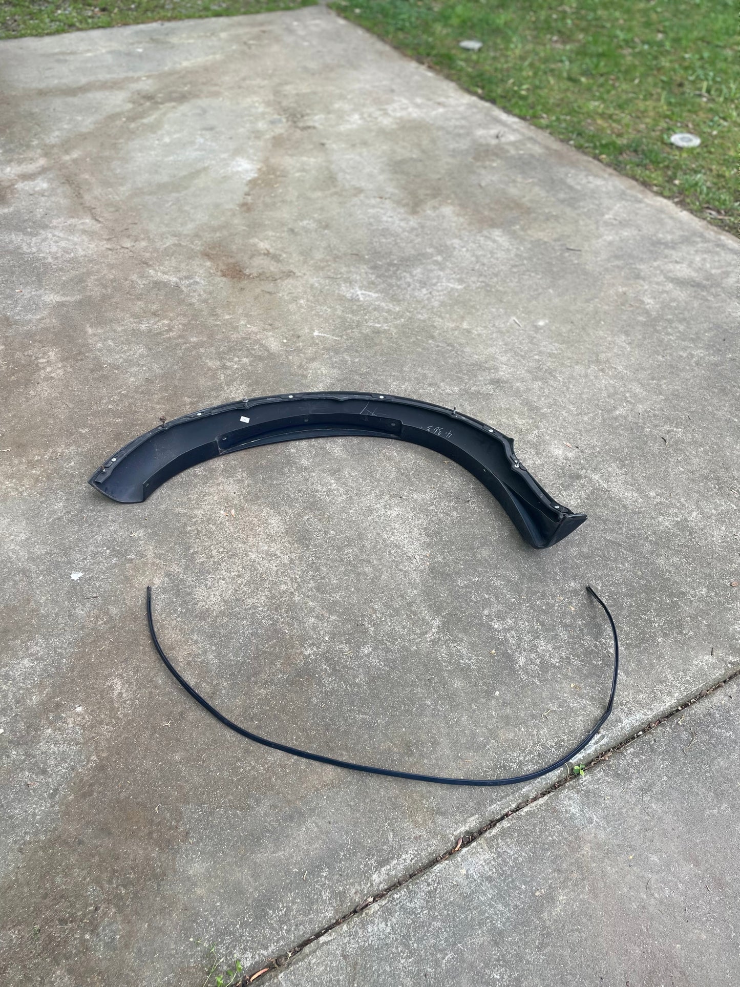 A blue OEM Front Right Passenger ZR2 Fender Flare Extension by General Motors for 1994-2005 Chevy S10 and GMC Sonoma lies on a concrete driveway, with a thin strip nearby and green grass in the background.