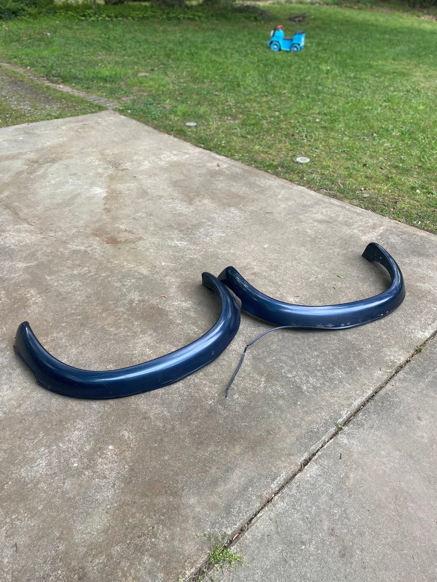A pair of blue OEM Rear ZR2 Bed Flare Extensions by General Motors for 1994-2004 Chevy S10 or GMC Sonoma are shown on a concrete driveway, with grass and a blue toy car in the background.