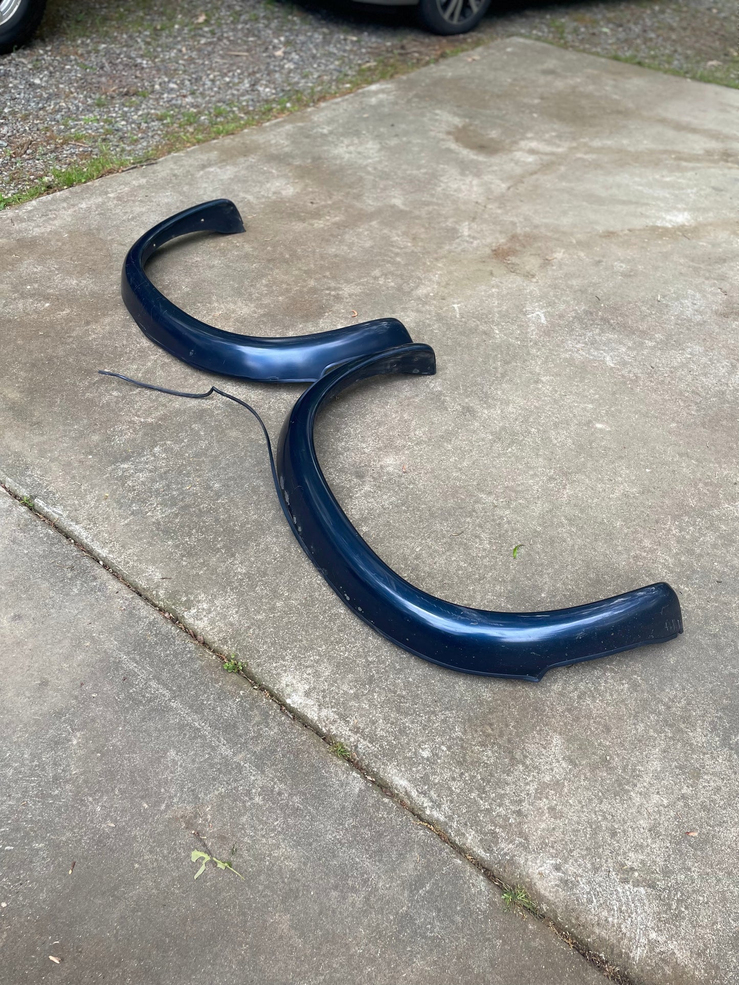 A pair of blue OEM Rear ZR2 Bed Flares Extensions by General Motors for 1994-2004 Chevy S10 and GMC Sonoma lies on a concrete driveway, with a thin strip nearby—perfect fit for Chevrolet S10 ZR2 or GMC Sonoma Highrider owners.