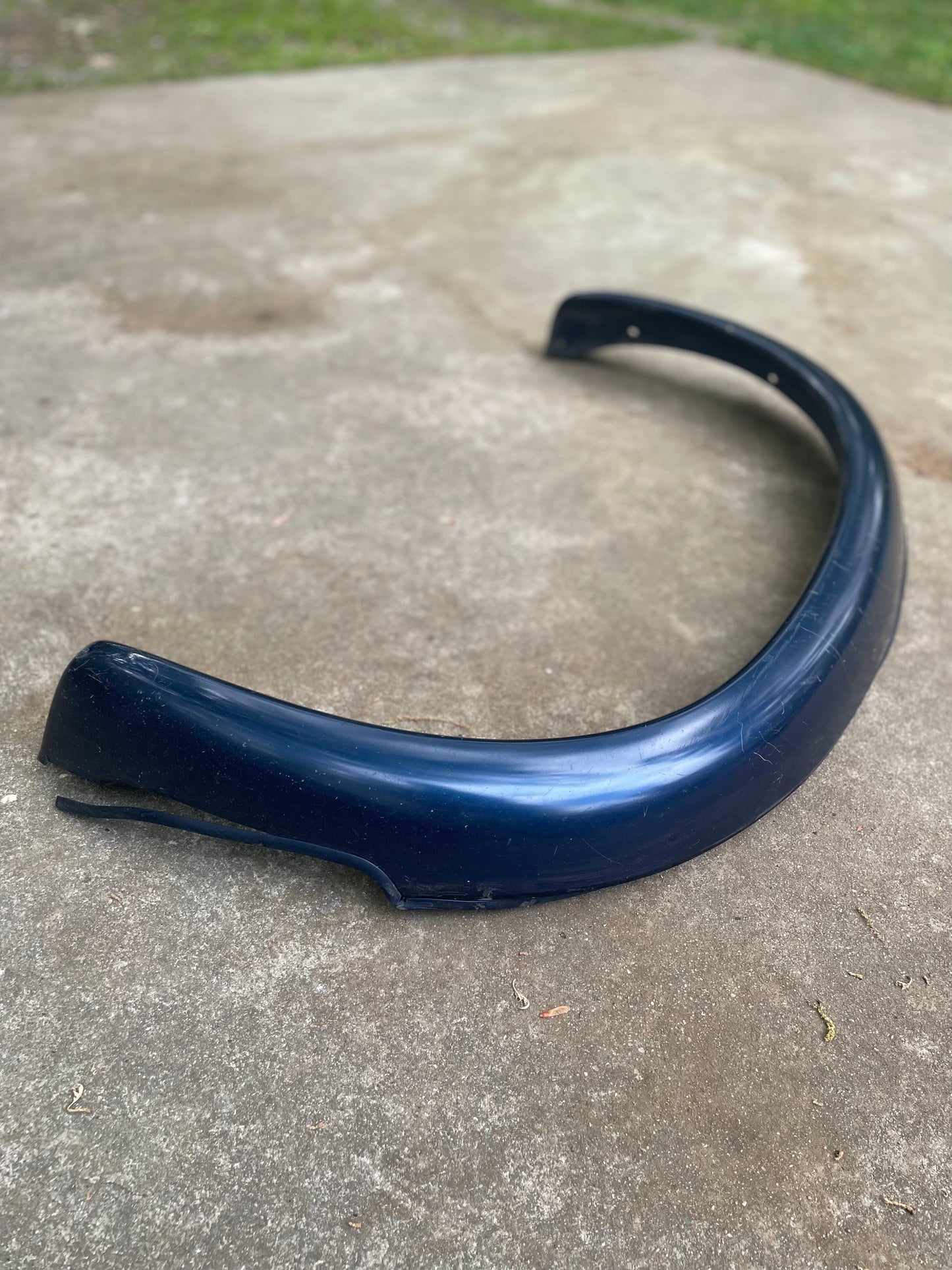 A pair of OEM Rear ZR2 Bed Flares Extensions in blue from General Motors for 1994-2004 Chevy S10 or GMC Sonoma lies outdoors on concrete, with grass in the background.