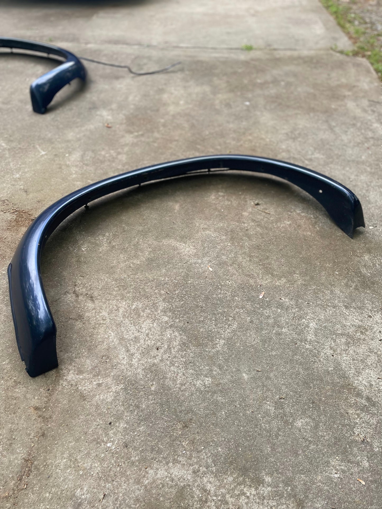 A pair of blue OEM rear ZR2 bed flares extensions for 1994-2004 Chevy S10 and GMC Sonoma by General Motors lies on a concrete driveway, with another similar part visible in the background.