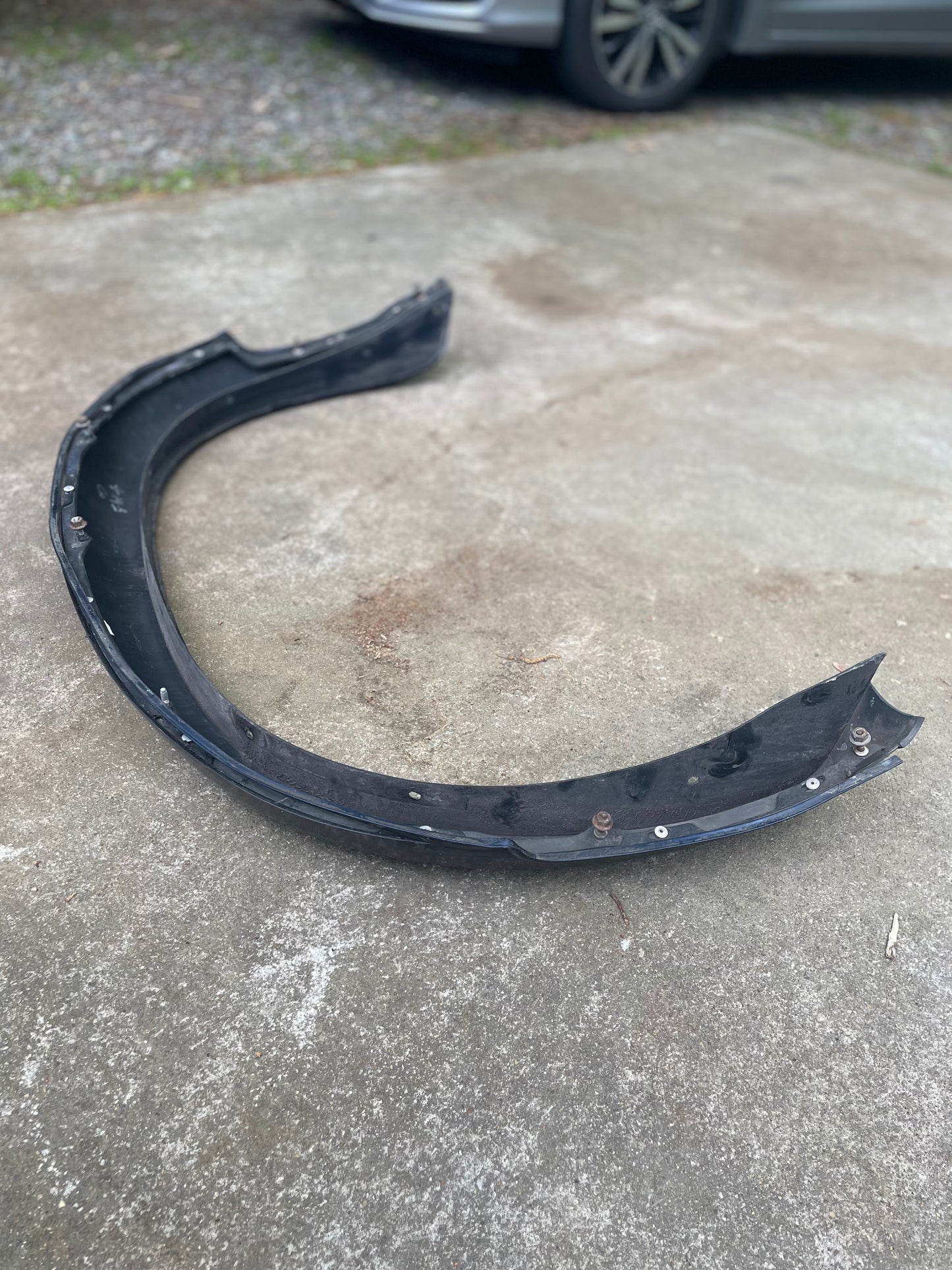 A blue, curved car part—General Motors OEM Pair Rear ZR2 Bed Flares Extension—rests on a concrete driveway. Designed for 1994-2004 Chevy S10 or GMC Sonoma models. A gray car and gravel are visible in the background.