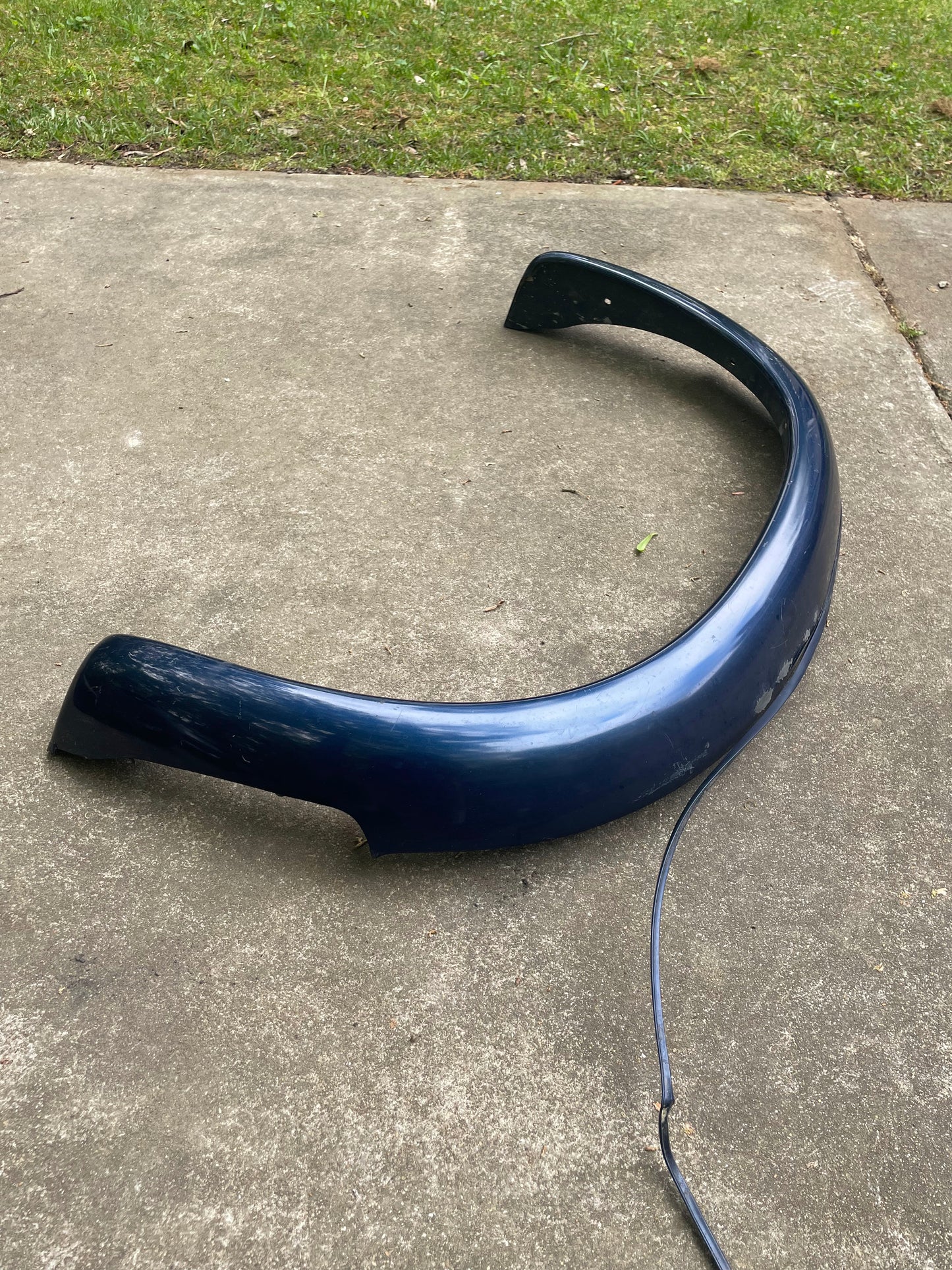 A blue OEM pair of General Motors Rear ZR2 Bed Flare Extensions for 1994-2004 Chevy S10/GMC Sonoma rests outdoors on concrete, with grass in the background and a black wire trailing beside them.