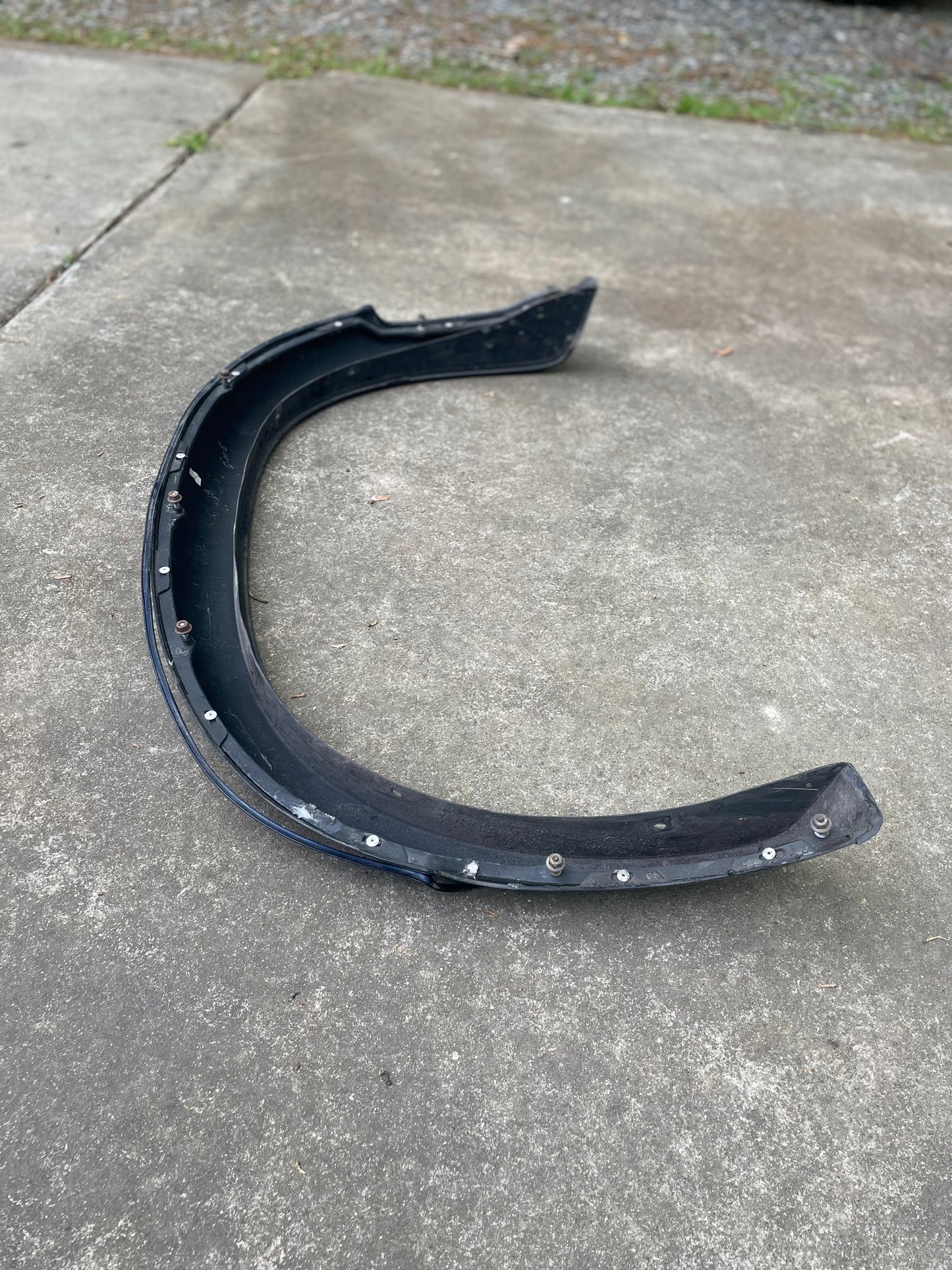 A blue OEM pair of General Motors rear ZR2 bed flares extensions for 1994-2004 Chevy S10 or GMC Sonoma rests on an outdoor concrete surface, with grass and gravel in the background.