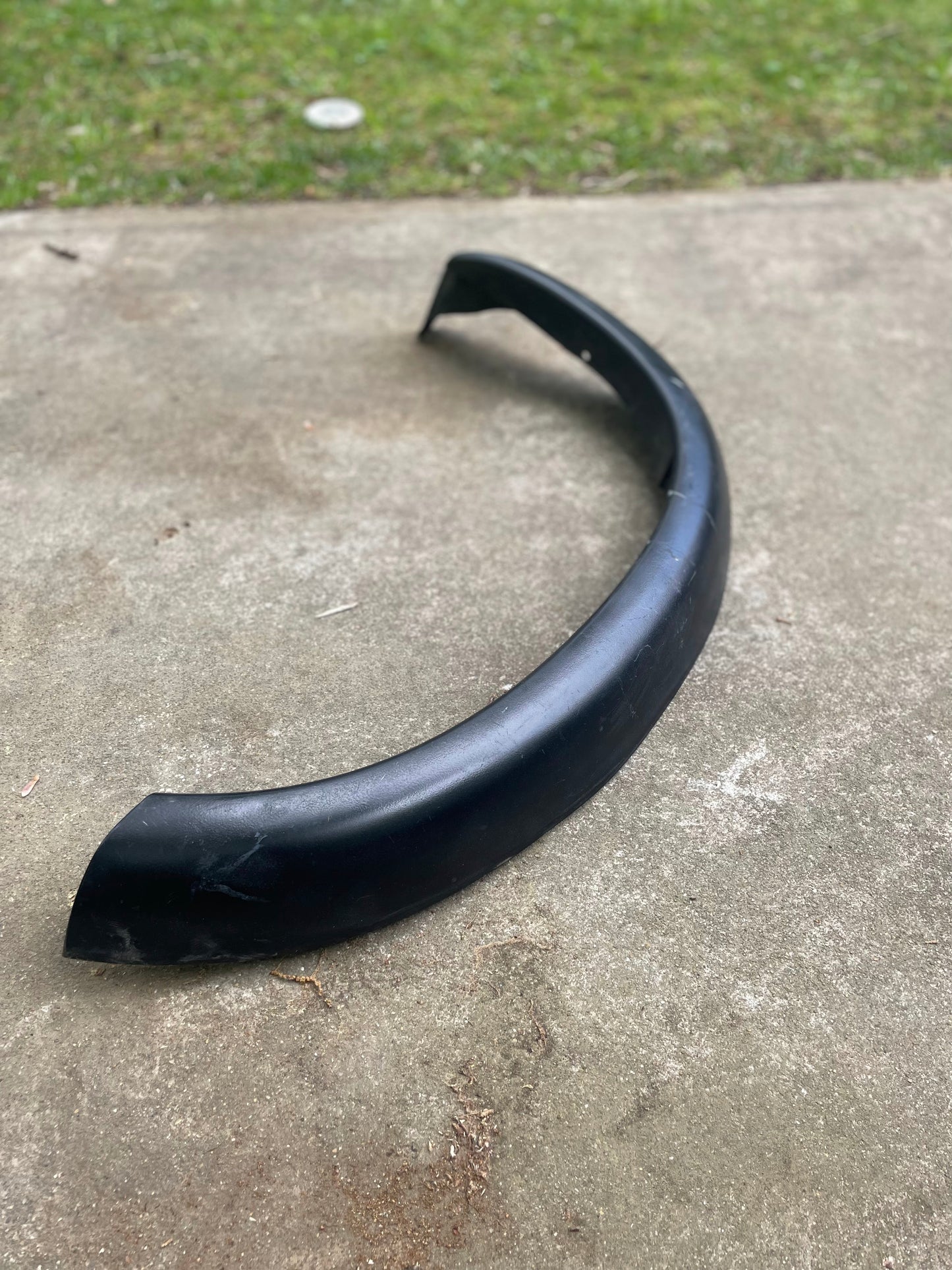 A General Motors OEM ZR2 Fender Flare Extension for 1994-2004 Chevy S10 or GMC Sonoma lies on a concrete surface, with grass visible in the background.