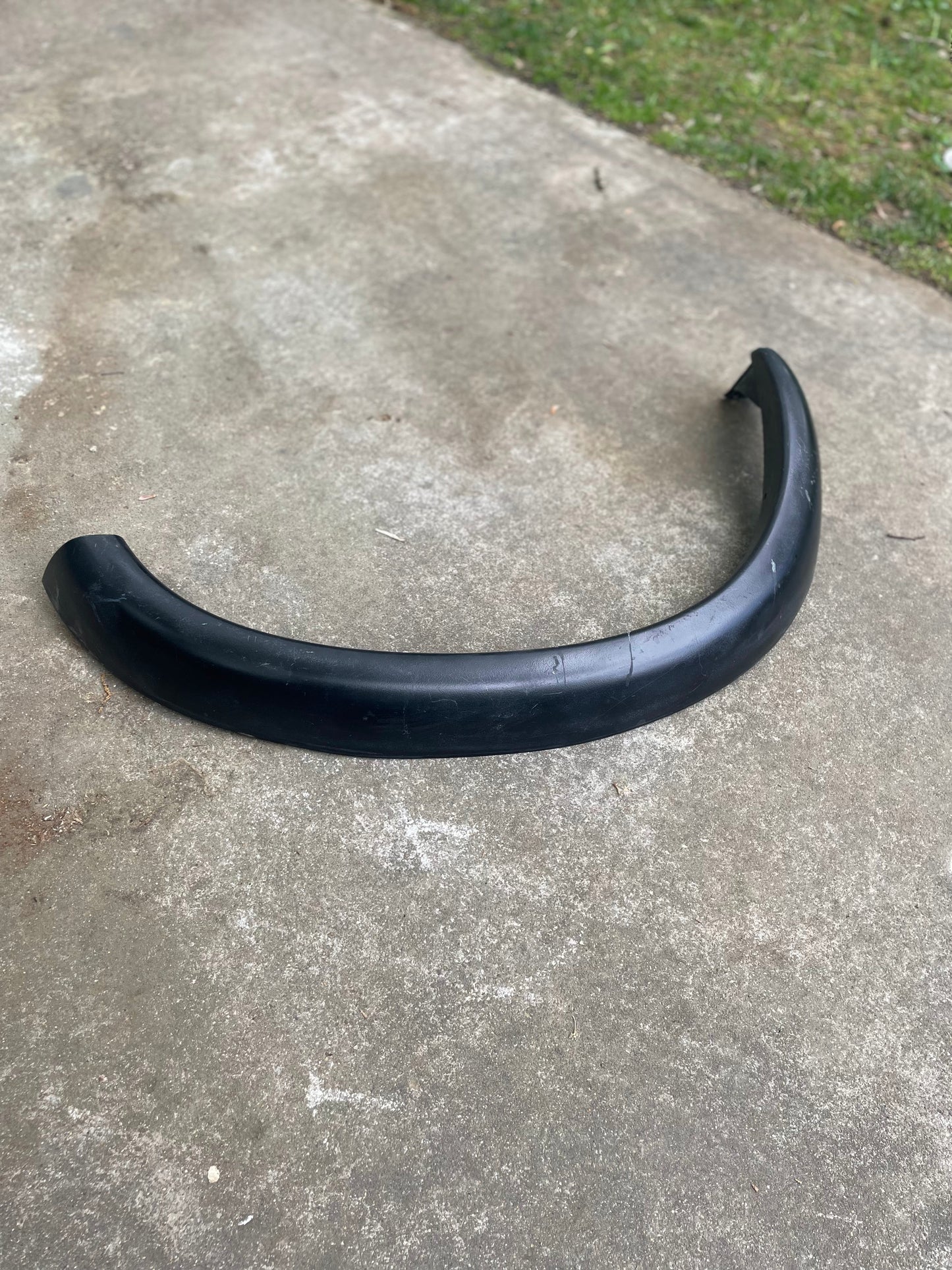 A black General Motors OEM Set ZR2 Fender Flares Extension for 1994-2004 Chevy S10 or GMC Sonoma lies on a concrete surface, with some grass in the background.