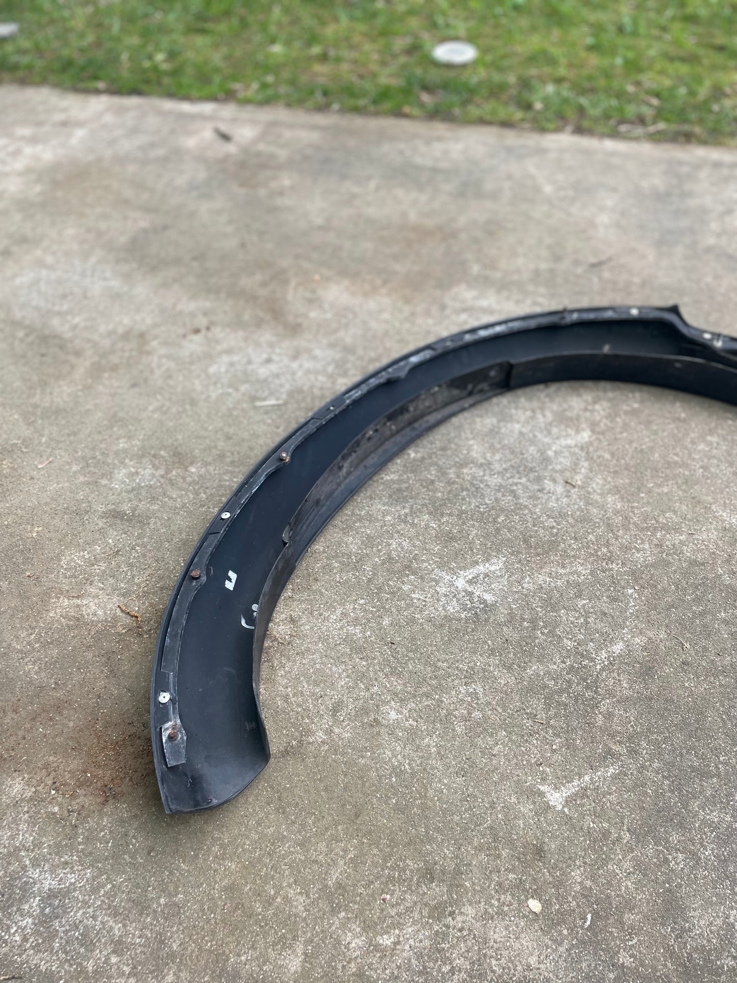 A black plastic OEM ZR2 fender flare extension by General Motors for 1994-2004 Chevy S10 or GMC Sonoma lies scratched and detached on a concrete surface outdoors, with grass visible in the background.