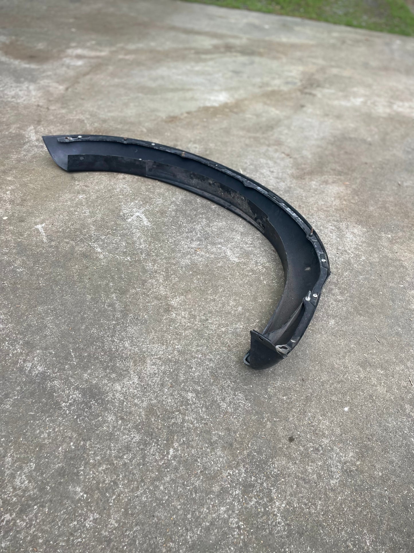 A black OEM Set ZR2 Fender Flare Extension by General Motors for 1994-2004 Chevy S10 or GMC Sonoma rests on rough gray concrete outdoors, with a blurred greenish background.