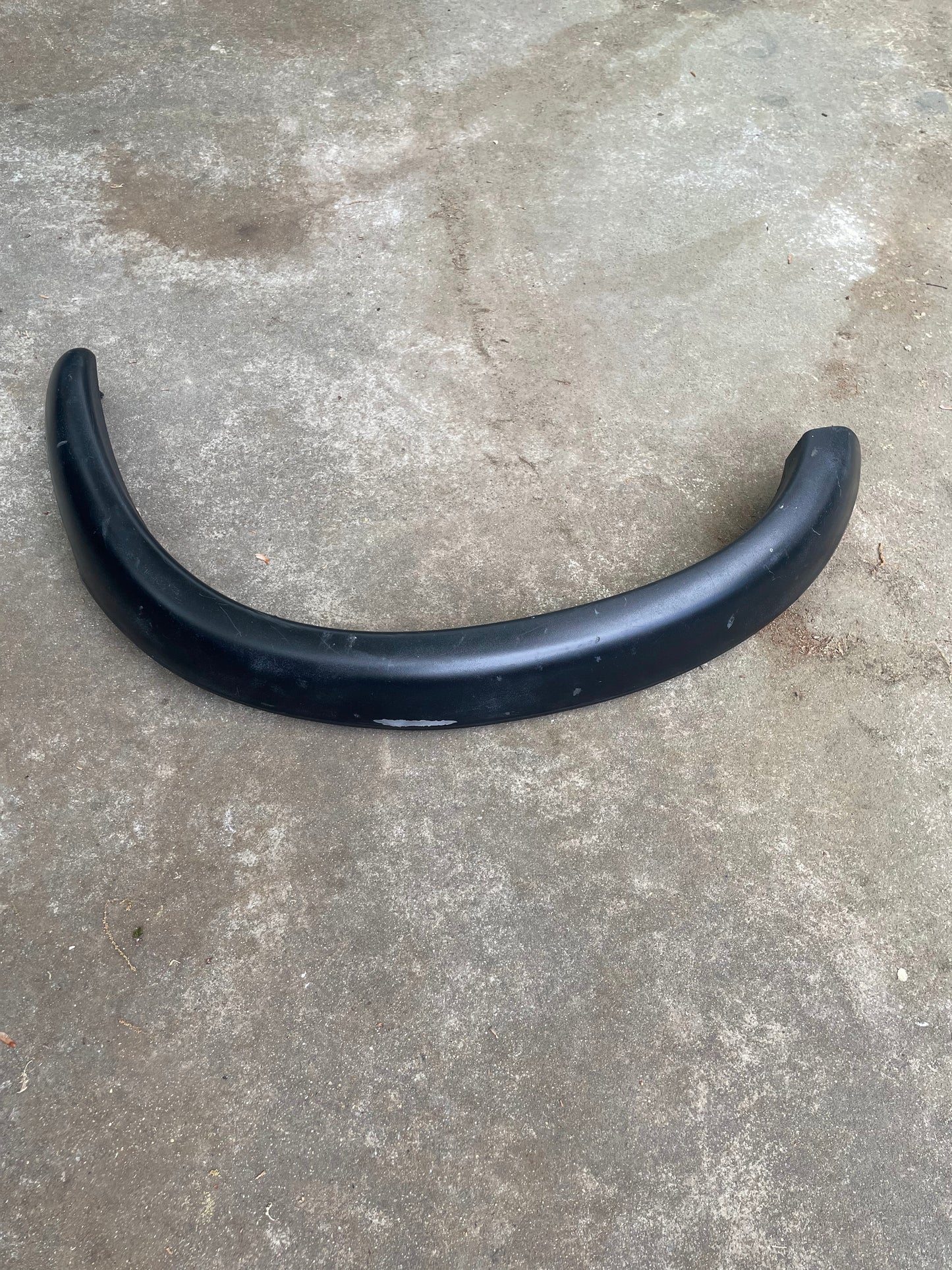 A black OEM General Motors ZR2 fender flare extension for 1994-2004 Chevy S10 or GMC Sonoma from the Set lies on stained concrete with light debris.