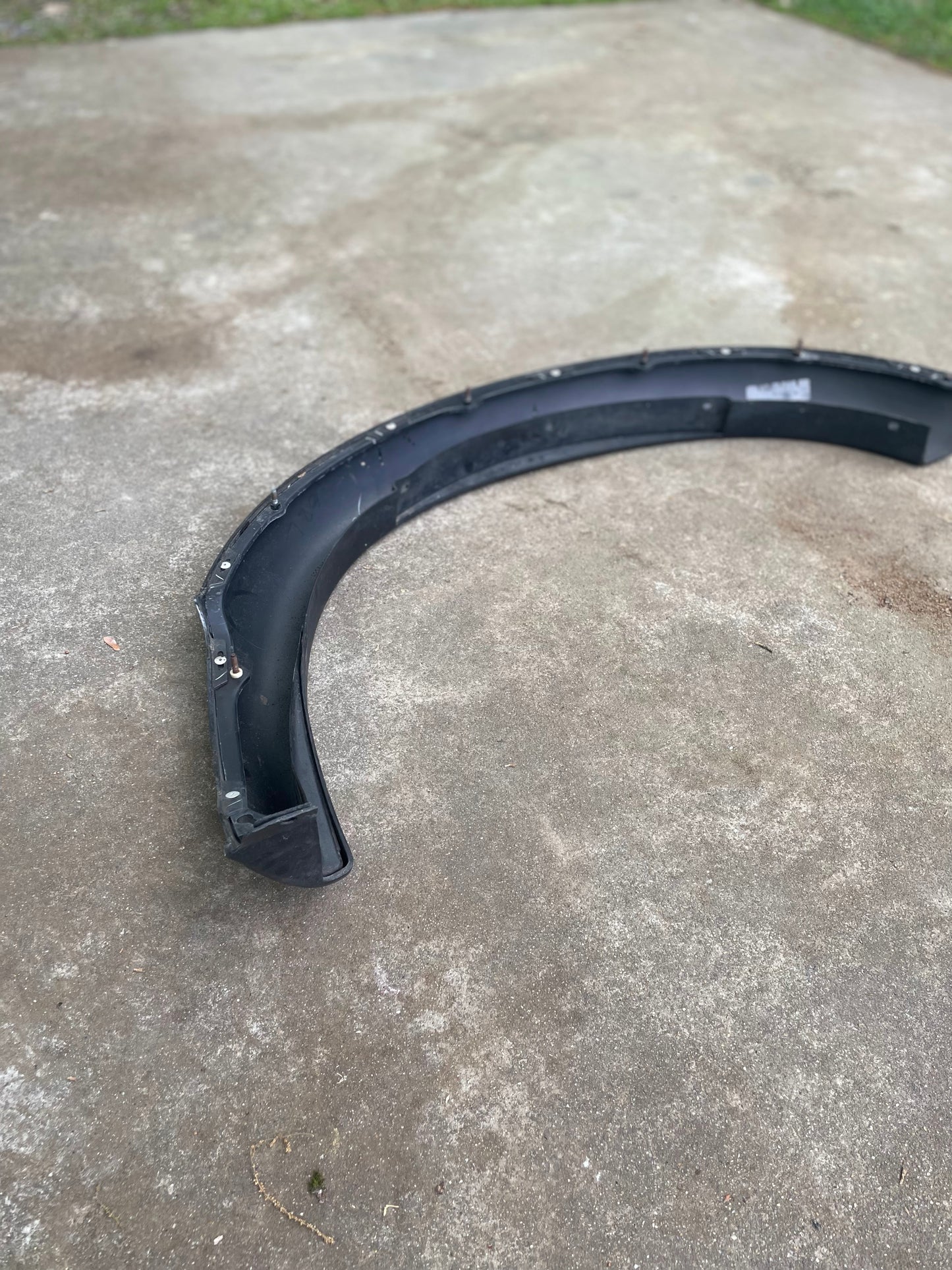 A black OEM General Motors ZR2 Fender Flare Extension for 1994-2004 Chevy S10 or GMC Sonoma is lying on a concrete surface outdoors, with grass visible in the background.