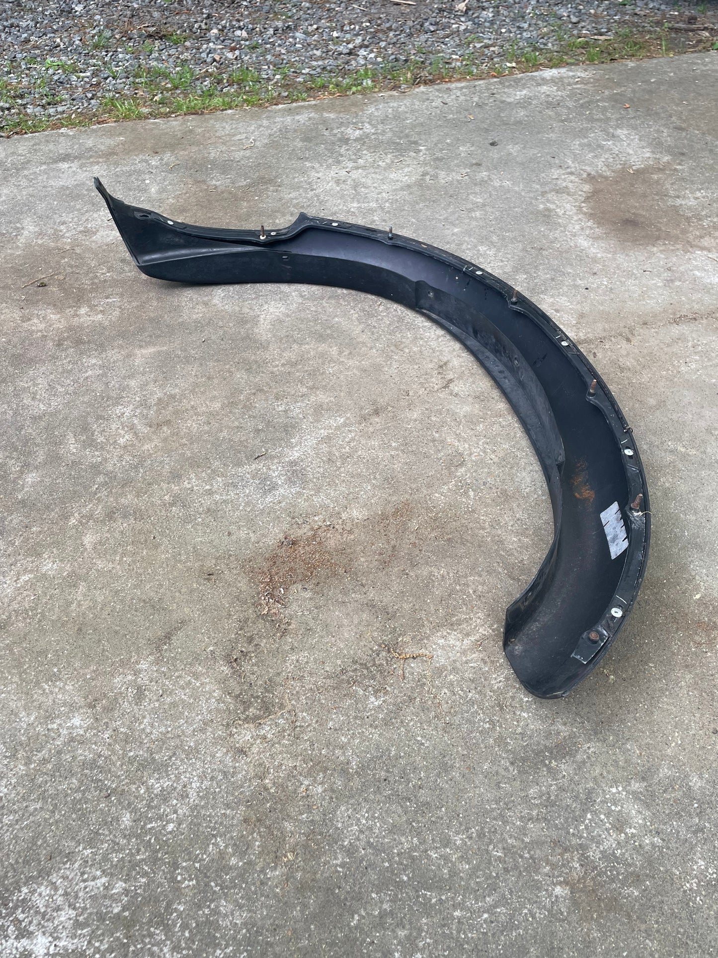 A black General Motors OEM ZR2 fender flare extension for 1994-2004 Chevy S10 or GMC Sonoma rests on concrete outdoors, with gravel and grass in the background.