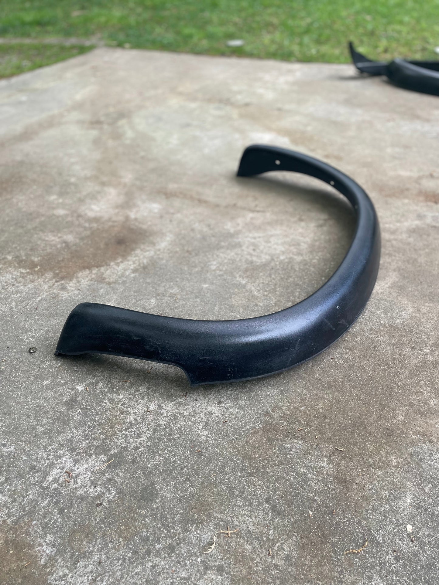 A General Motors OEM Set ZR2 Fender Flares Extension for 1994-2004 Chevy S10 or GMC Sonoma is shown outdoors on concrete, with grass behind it. Another matching fender flare extension is partially visible at the image’s top right.