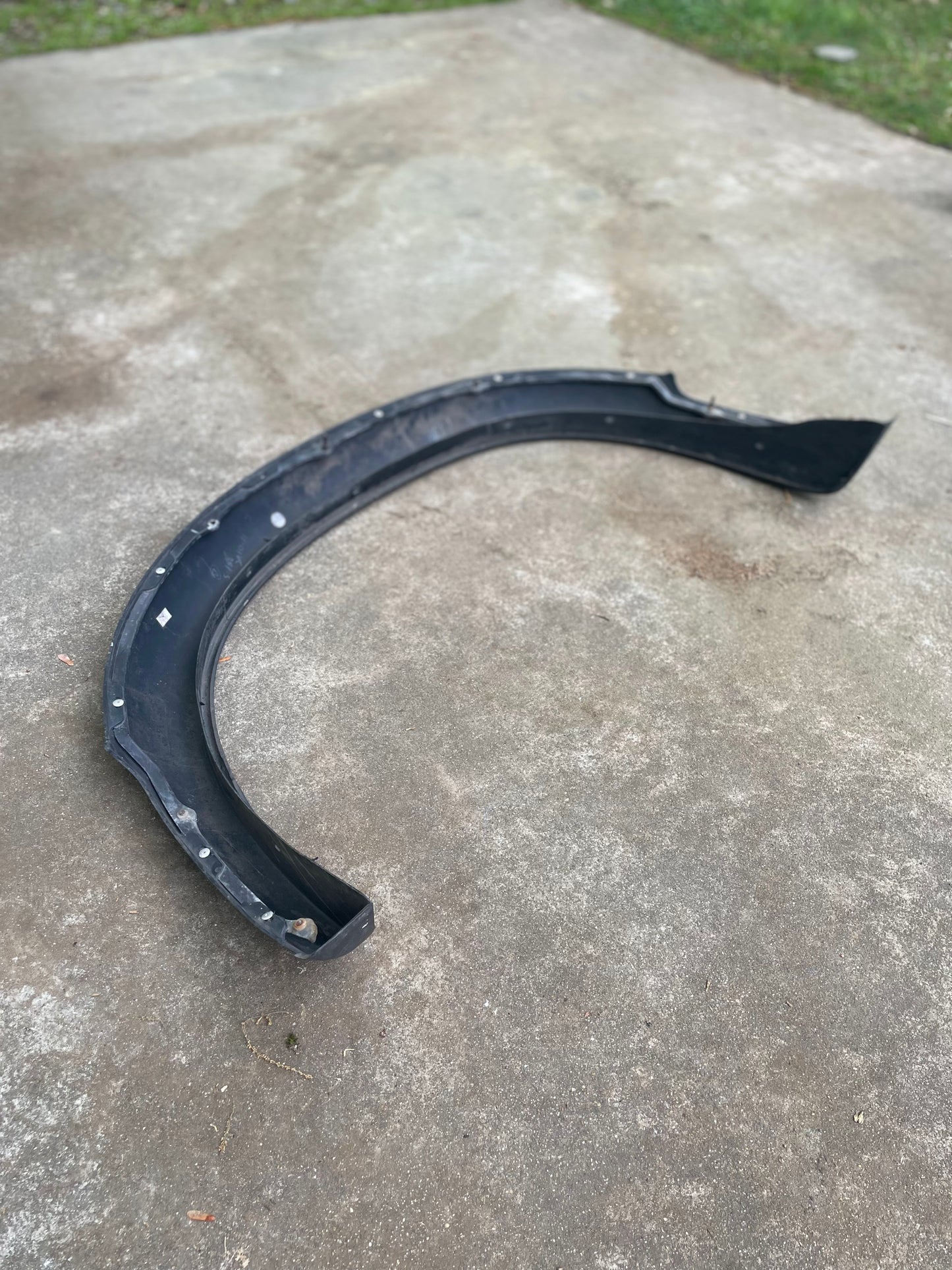 A black, curved bumper lies on concrete outdoors with grass behind—perfect for owners needing an OEM Set ZR2 Fender Flares Extension (1994-2004 Chevy S10, GMC Sonoma) by General Motors.