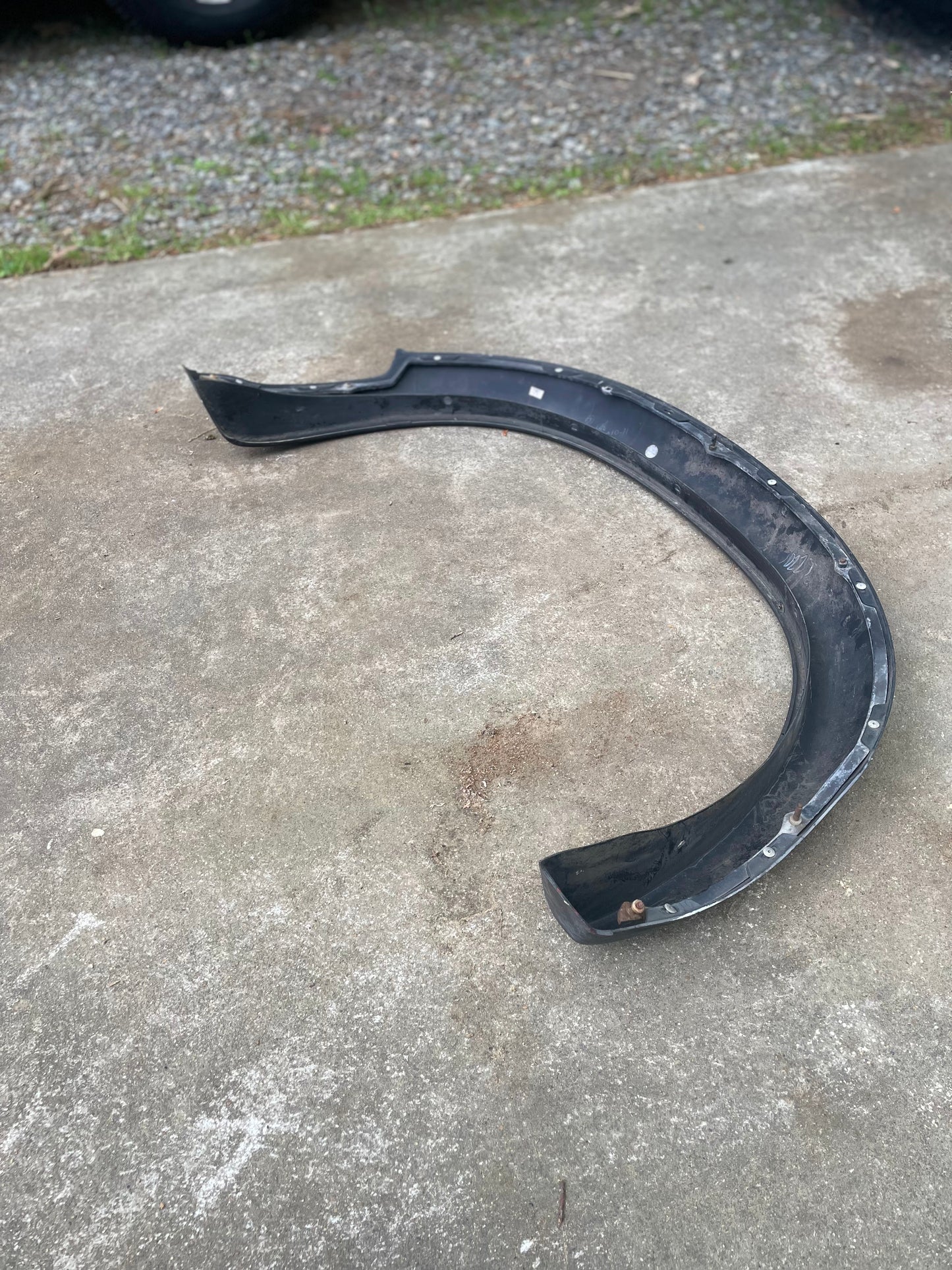 A curved, black plastic General Motors OEM ZR2 fender flare extension for a 1994-2004 Chevy S10 or GMC Sonoma lies on a concrete driveway with some grass and gravel in the background.