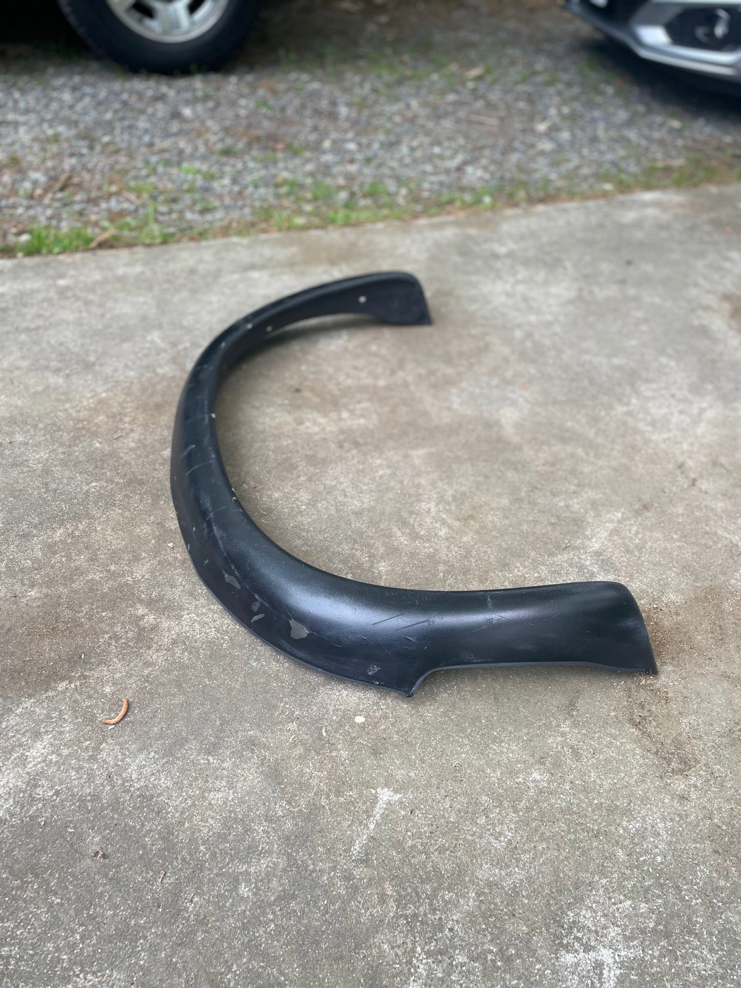 An OEM General Motors ZR2 fender flare extension for 1994-2004 Chevy S10 or GMC Sonoma rests on a concrete driveway, with part of a GMC Sonoma and some gravel in the background.
