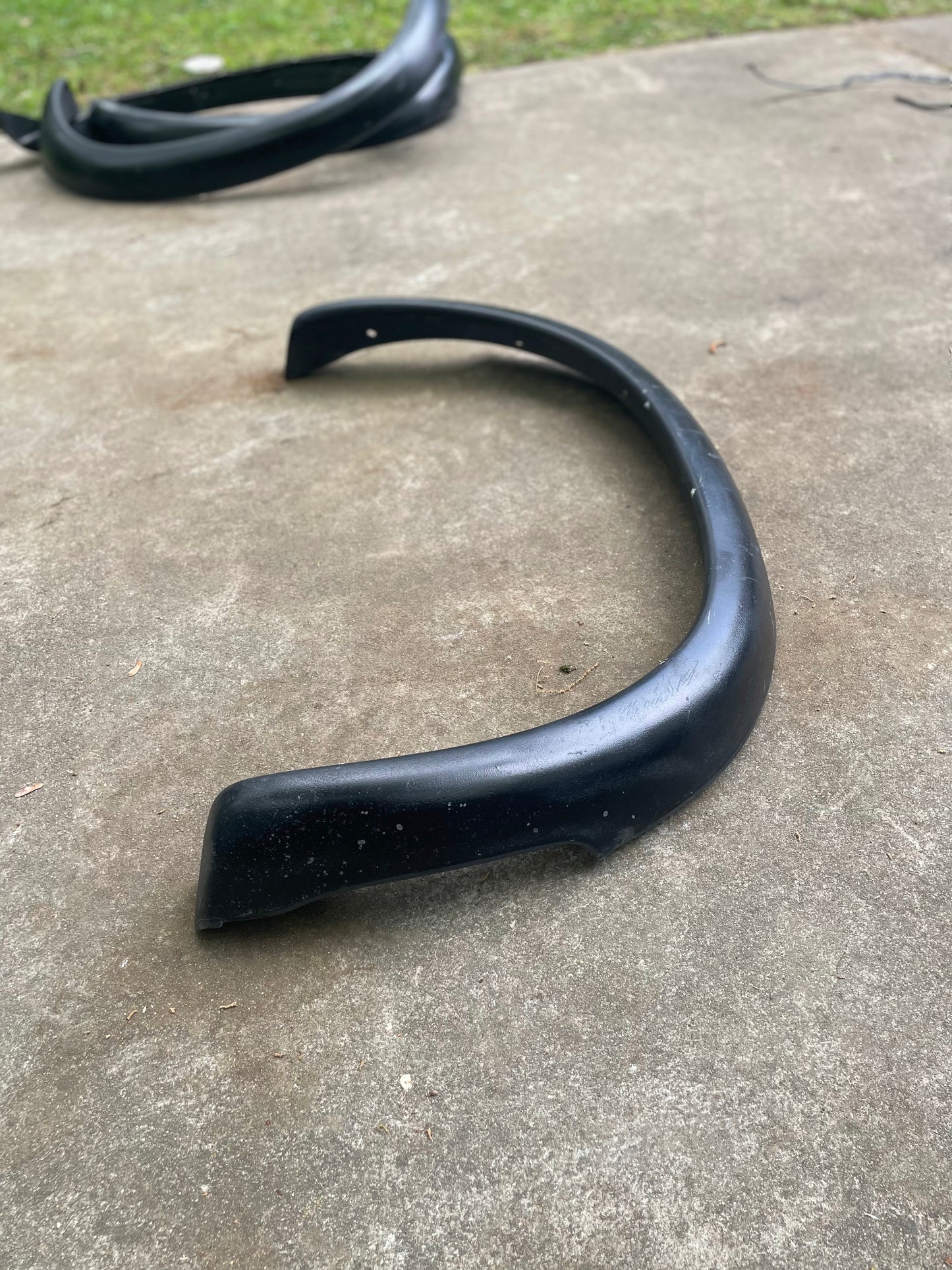 A General Motors OEM Set ZR2 Fender Flares Extension for 1994-2004 Chevy S10, GMC Sonoma lies on a concrete surface outdoors with grass in the background; another fender flare is visible in the upper left corner.