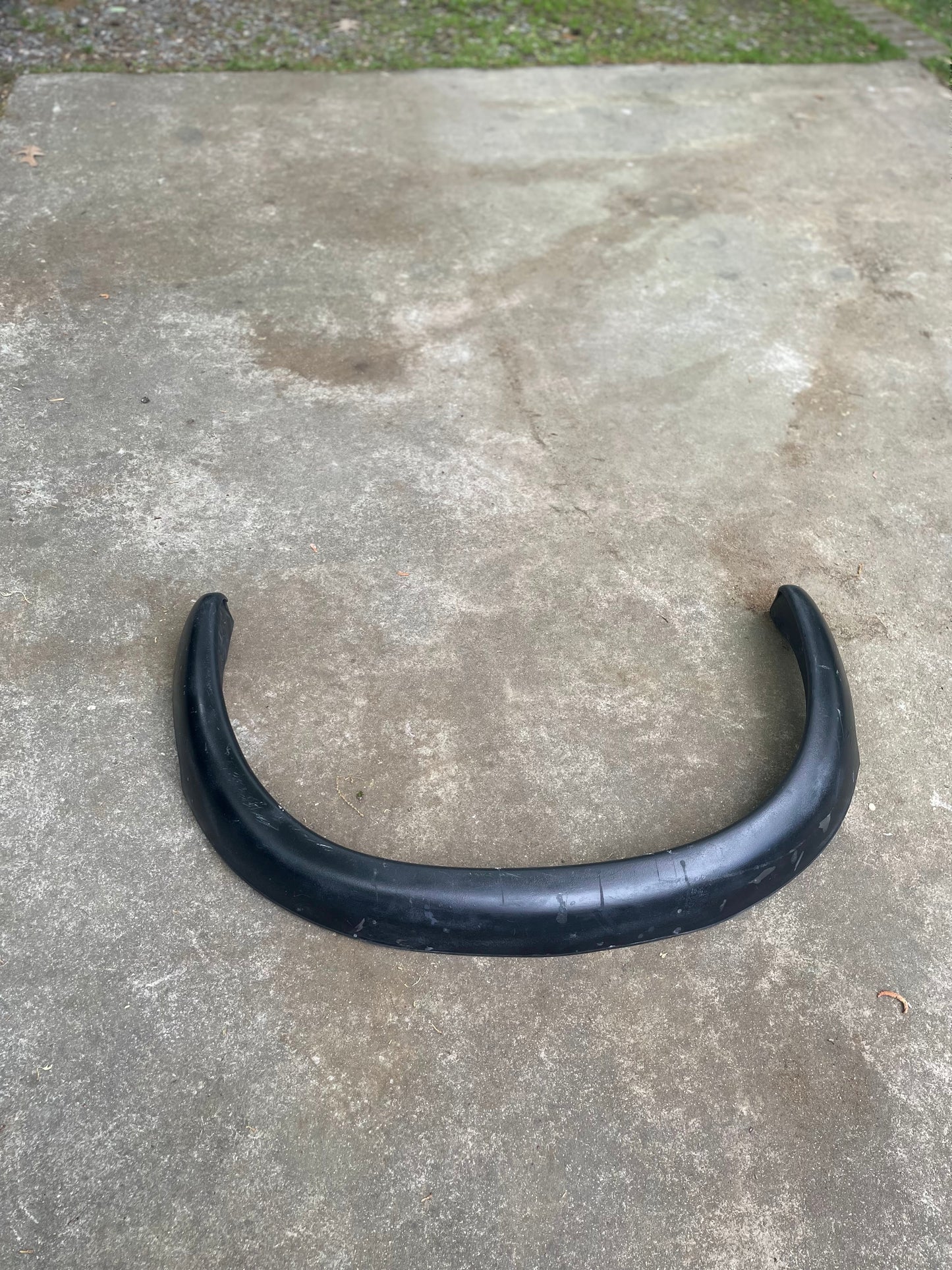 A General Motors OEM Set ZR2 Fender Flares Extension for 1994-2004 Chevy S10/GMC Sonoma lies on an outdoor concrete surface, with grass and gravel in the background.