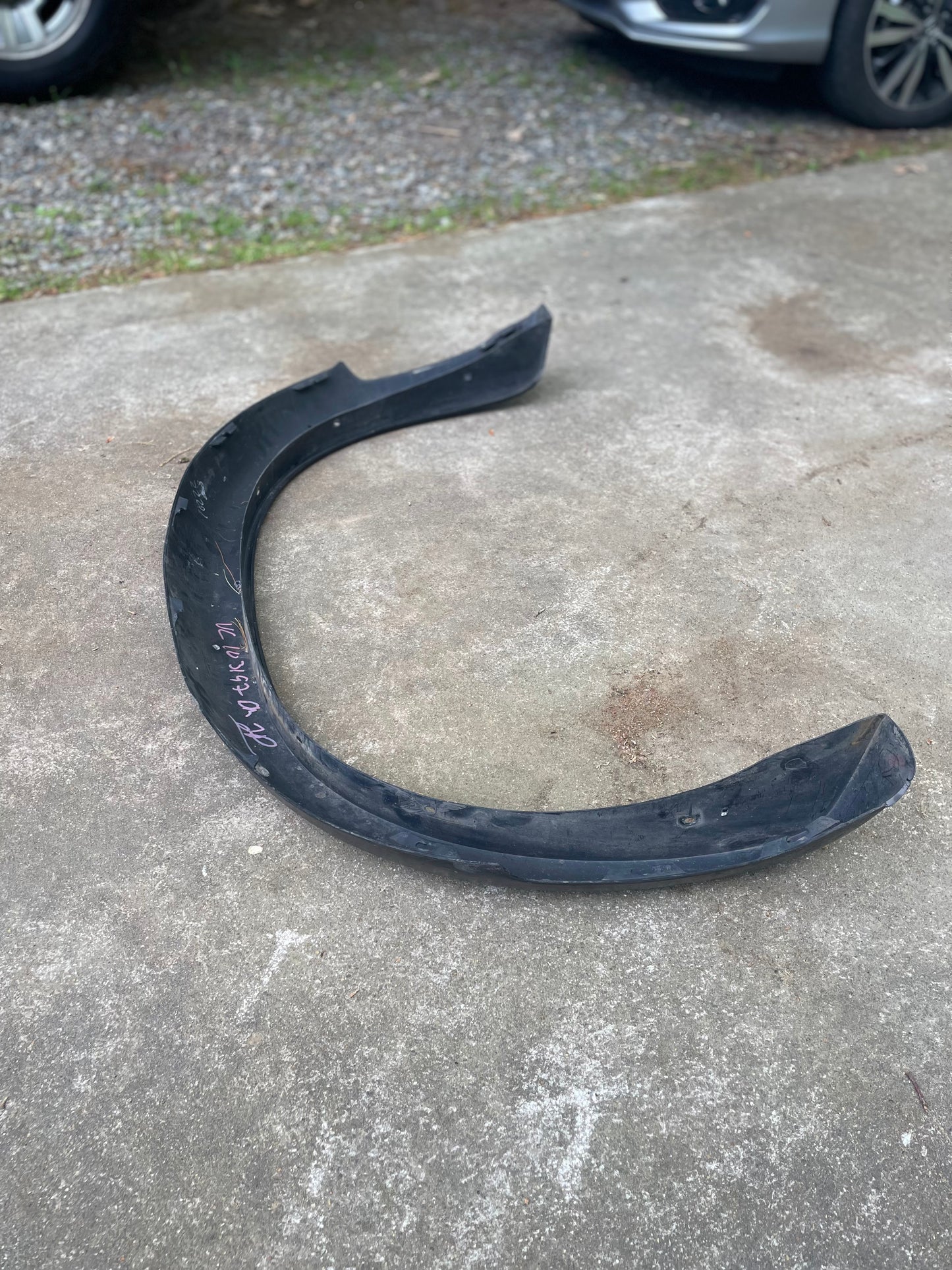 A black OEM Set ZR2 Fender Flares Extension by General Motors for 1994-2004 Chevy S10 or GMC Sonoma sits on a concrete driveway, surrounded by gravel and parked cars.