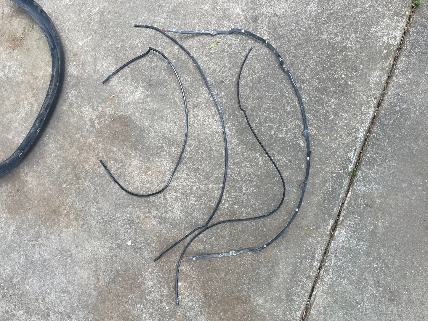 Three strips of broken black rubber and a partial circle lay on rough concrete—likely remnants from a General Motors OEM Set ZR2 Fender Flares Extension for 1994-2004 Chevy S10 or GMC Sonoma, not just a bicycle inner tube.