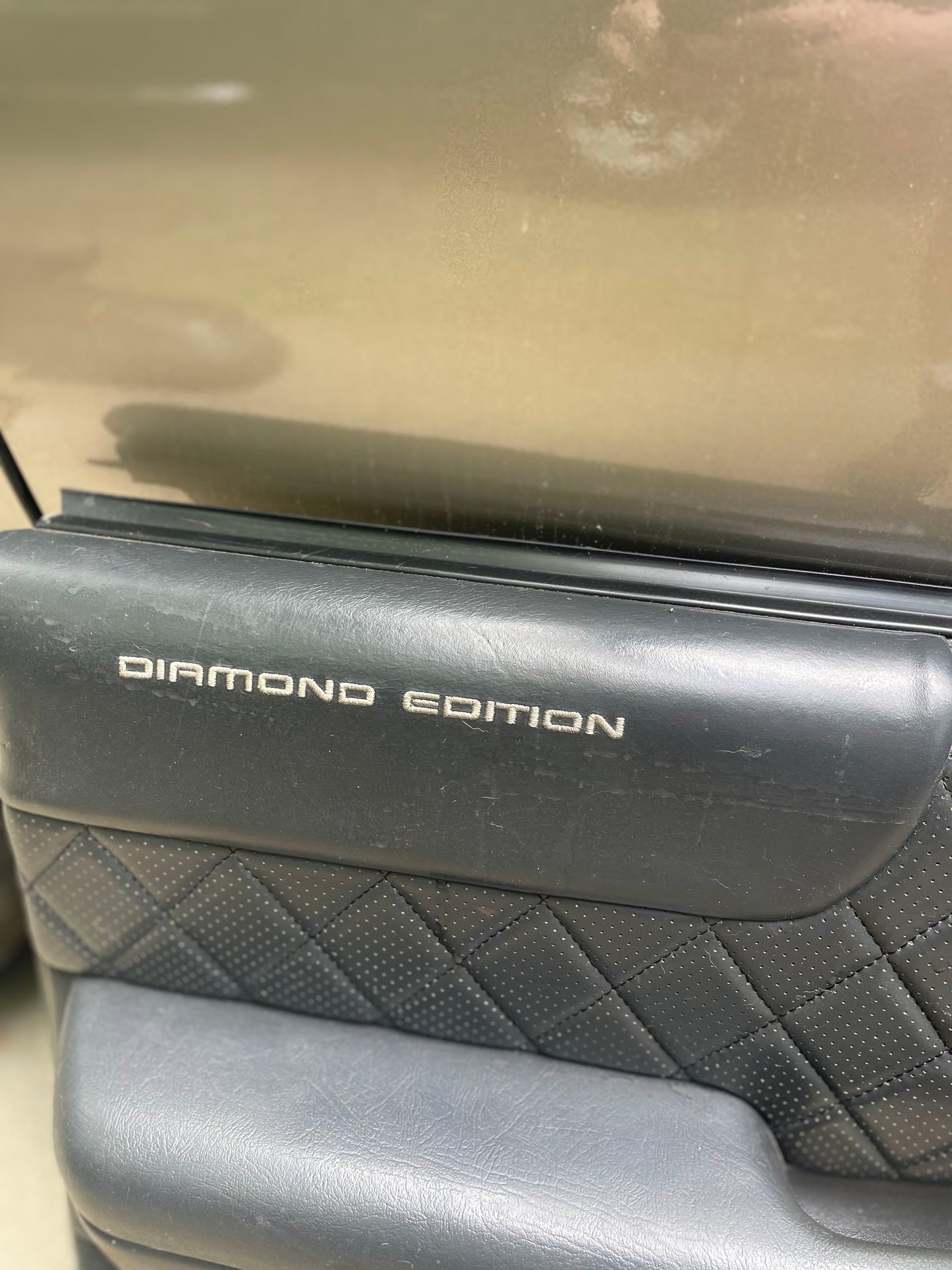 Close-up of General Motors OEM dark gray front power leather diamond door panels for 1998-2005 Chevy S10/GMC Sonoma, seen here installed with the vehicle’s exterior visible through the window.