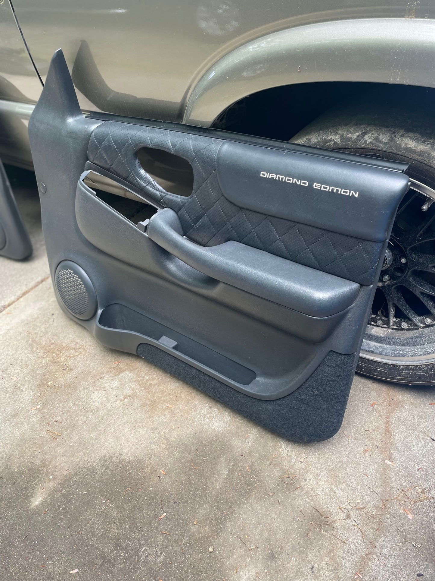A pair of General Motors OEM front power leather Diamond door panels in dark gray, designed for 1998-2005 Chevy S10 and GMC Sonoma, rests on the ground next to a vehicle—an upgrade over standard factory S10 interior panels.