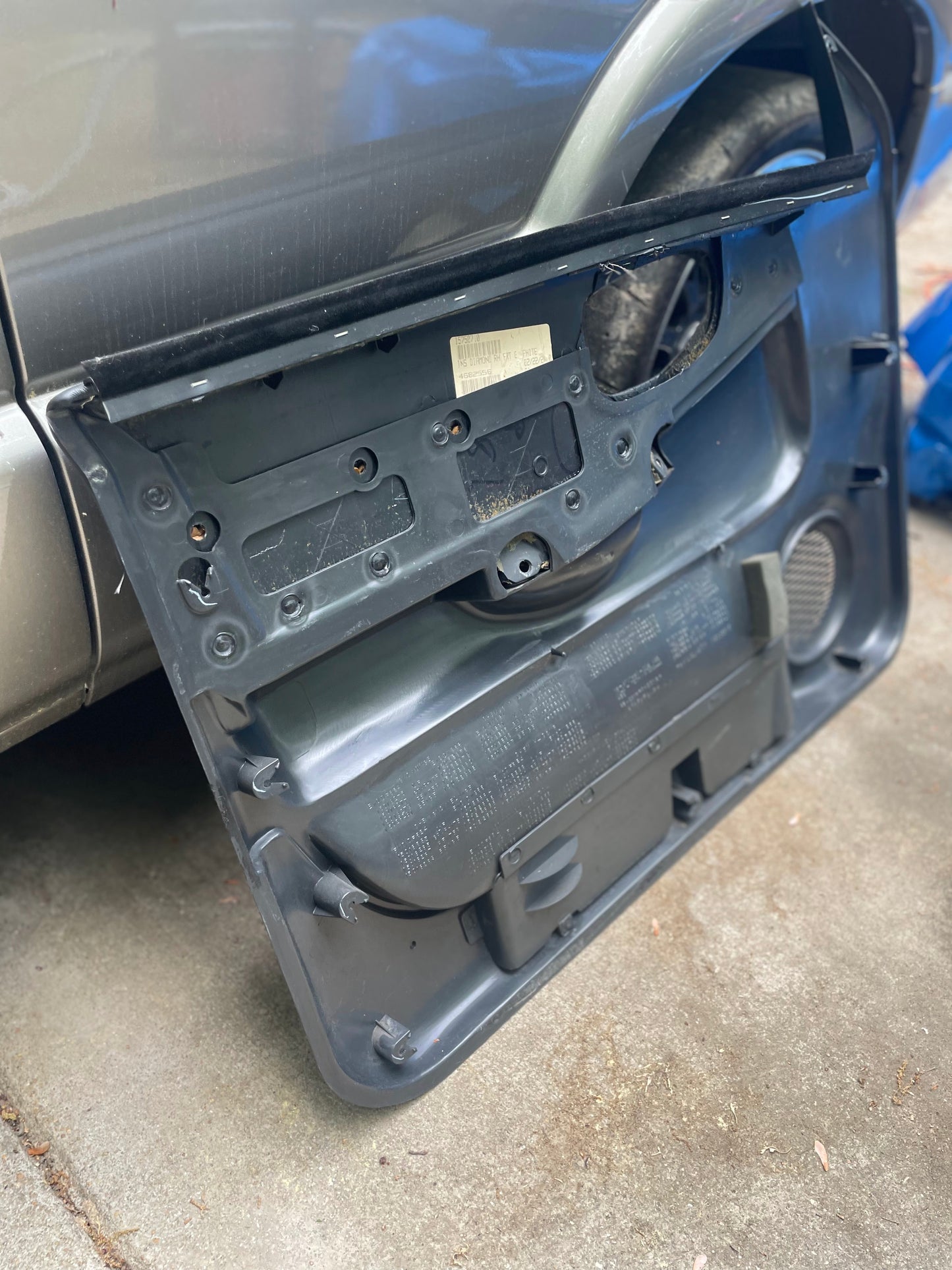 A pair of OEM General Motors dark gray leather power door panels for 1998-2005 Chevy S10/GMC Sonoma is shown, detached to display interior components and wiring, leaning against a silver vehicle on concrete.