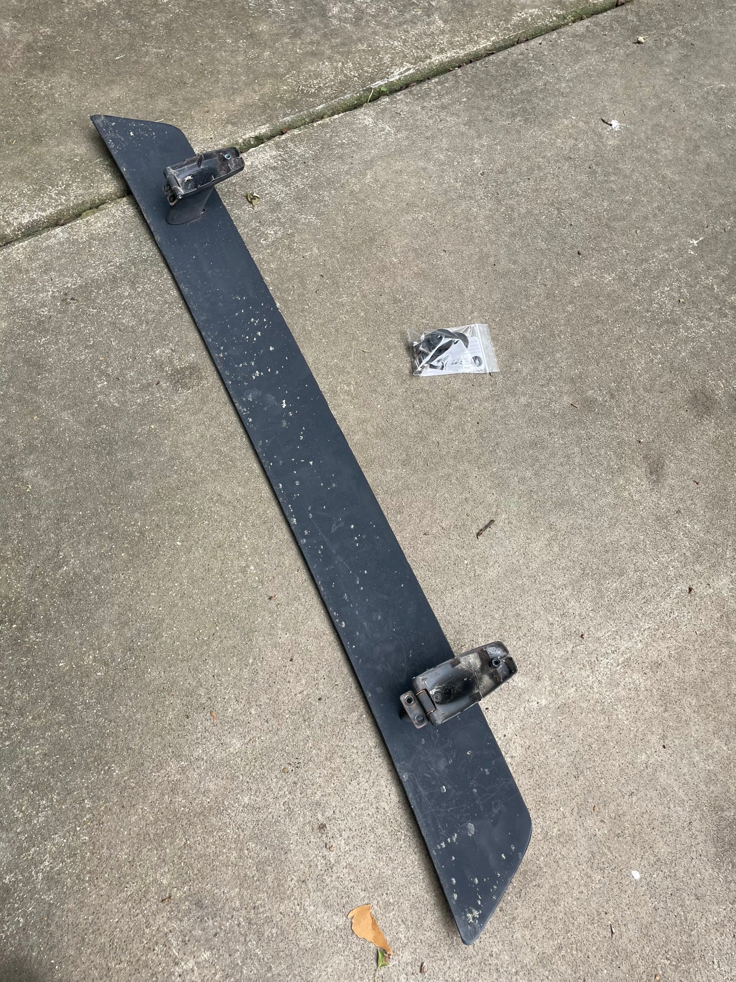 A General Motors OEM Rear Hatch Hinges with Spoiler Wing for 1983-1994 Chevrolet S10 Blazer is shown on concrete with two mounting brackets and a sealed hardware bag, indicating fitment for Chevy S10 Blazer rear glass upper hinges.