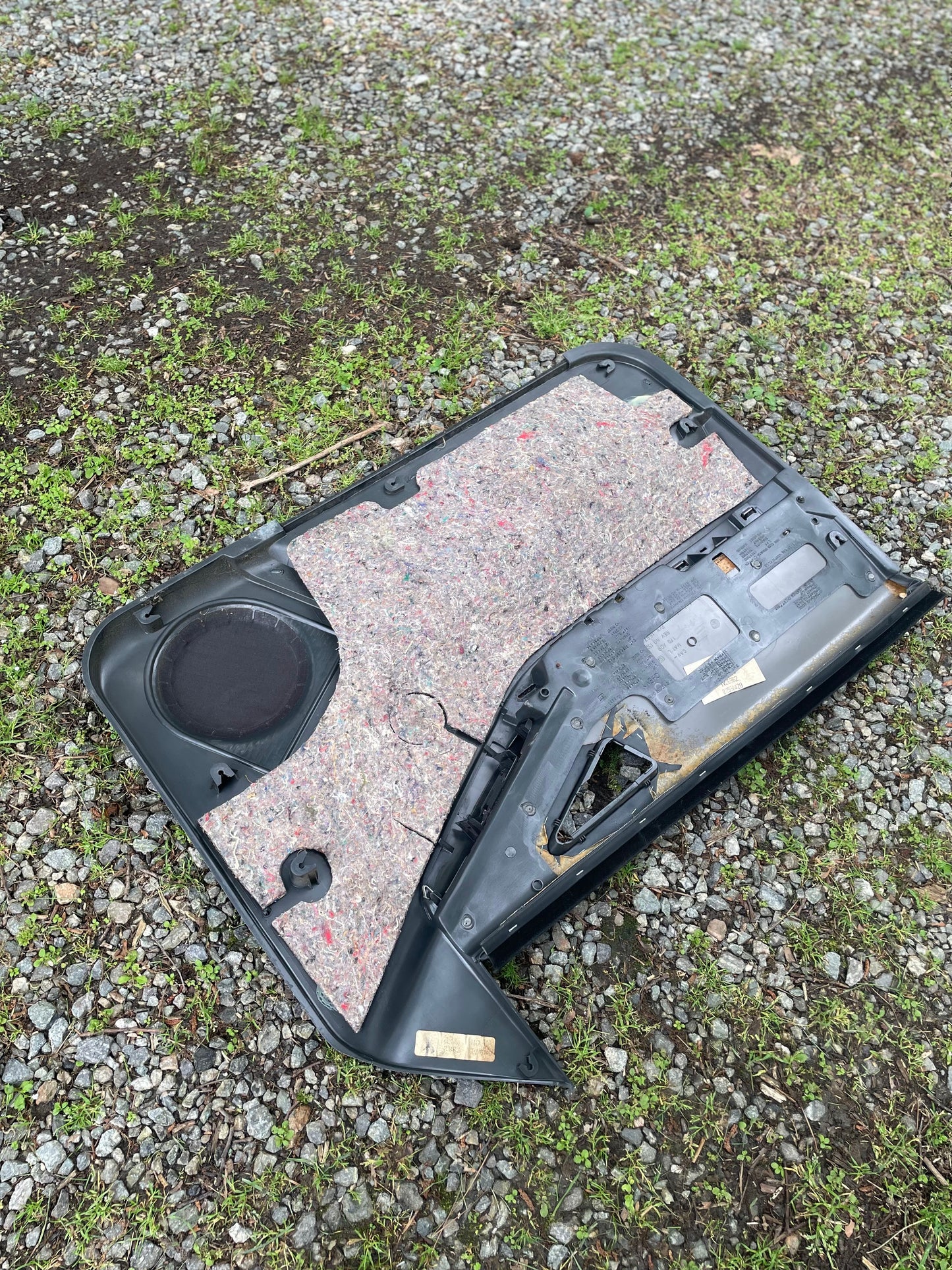 A pair of OEM General Motors dark gray front power door panels with woodgrain trim for 1994-1997 Chevy S10 and GMC Sonoma is lying face up on gravel and grass outdoors, insulation and wiring visible, angled on the ground.