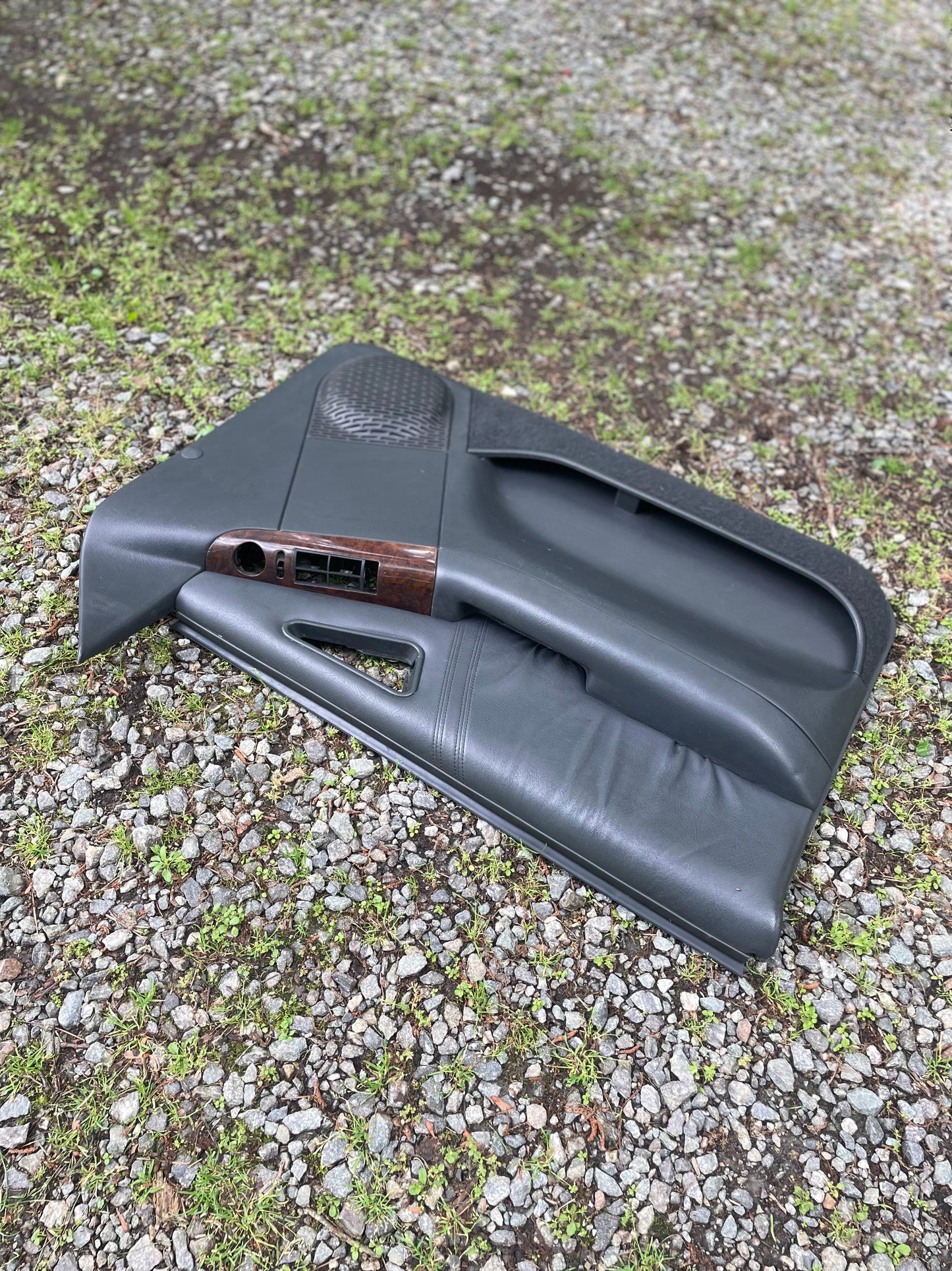A pair of OEM General Motors front power door panels in dark gray with woodgrain for 1994-1997 Chevy S10 and GMC Sonoma lies on gravel and grass outdoors.