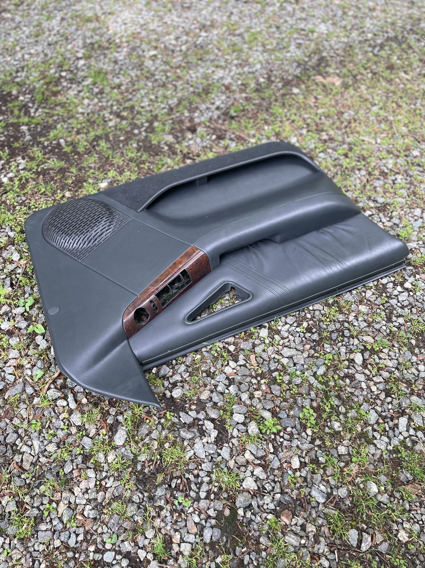 A pair of OEM General Motors dark gray front power door panels with woodgrain trim for 1994-1997 Chevy S10 and GMC Sonoma, shown outdoors with exposed speaker and handle areas, some components missing.